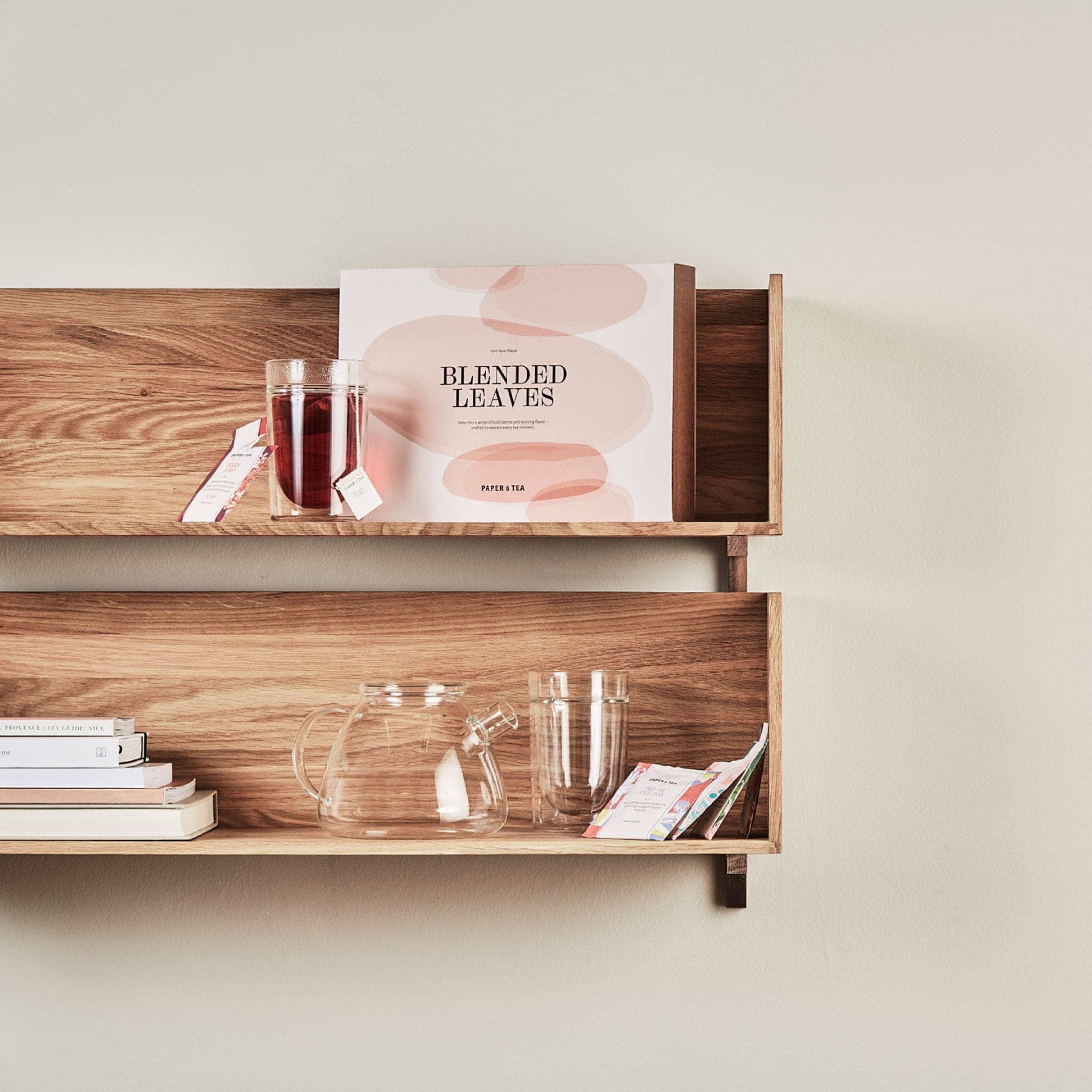 Elegantes Wandregal mit Tee, Glasbecher, Stadtführer, Teekrug und bunten Teebeuteln.