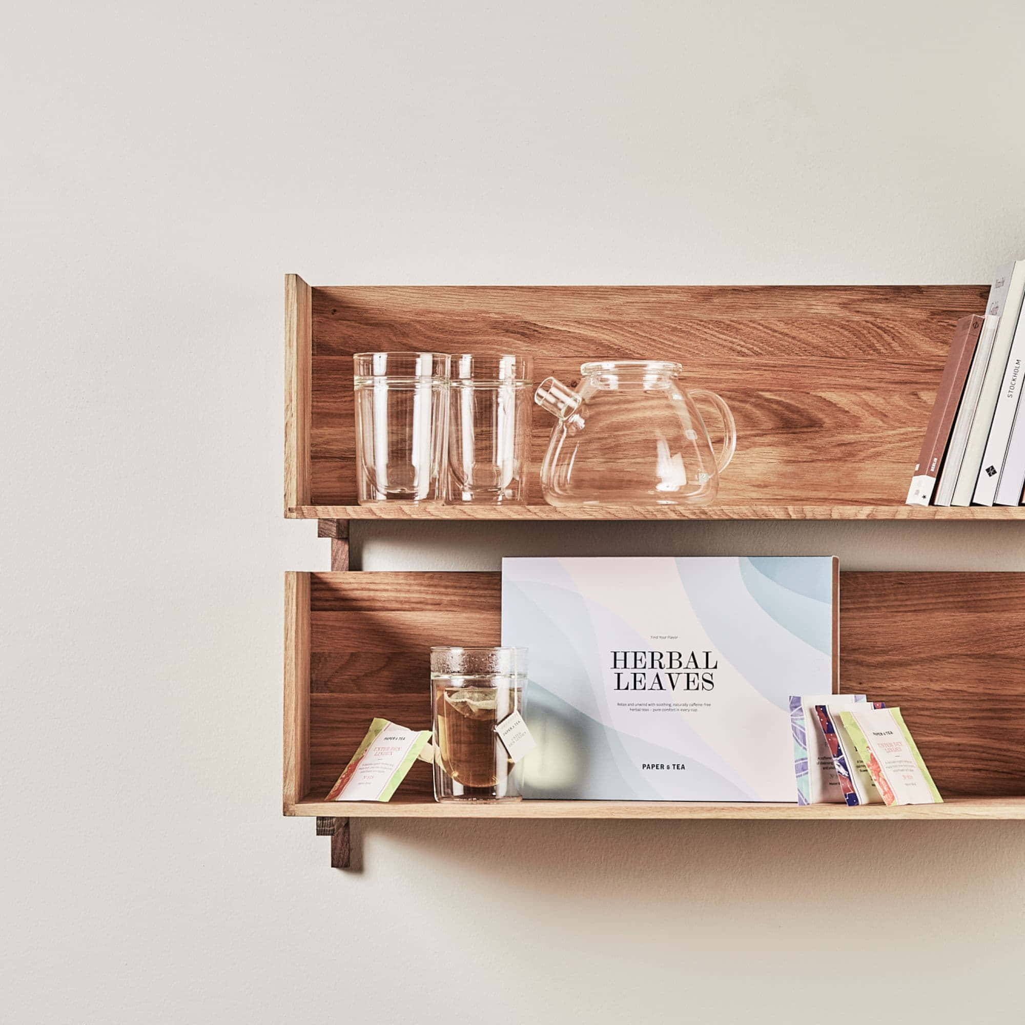 Minimalistisches Wandregal mit Glasgeschirr, Teekanne, Büchern und Paper & Tea Kräutertee-Verpackung.
