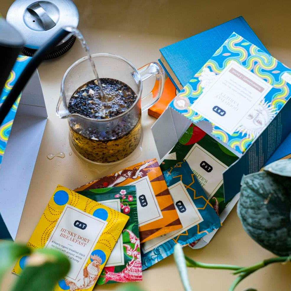 Glaskrug mit heißem Wasser umgeben von P & T Teepackungen, darunter HUNKY DORY BREAKFAST Bio-Schwarztee.