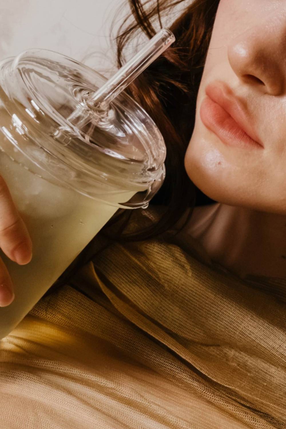 Person mit klarer Haut hält durchsichtigen Becher mit eisgekühltem grünen Getränk und Strohhalm.