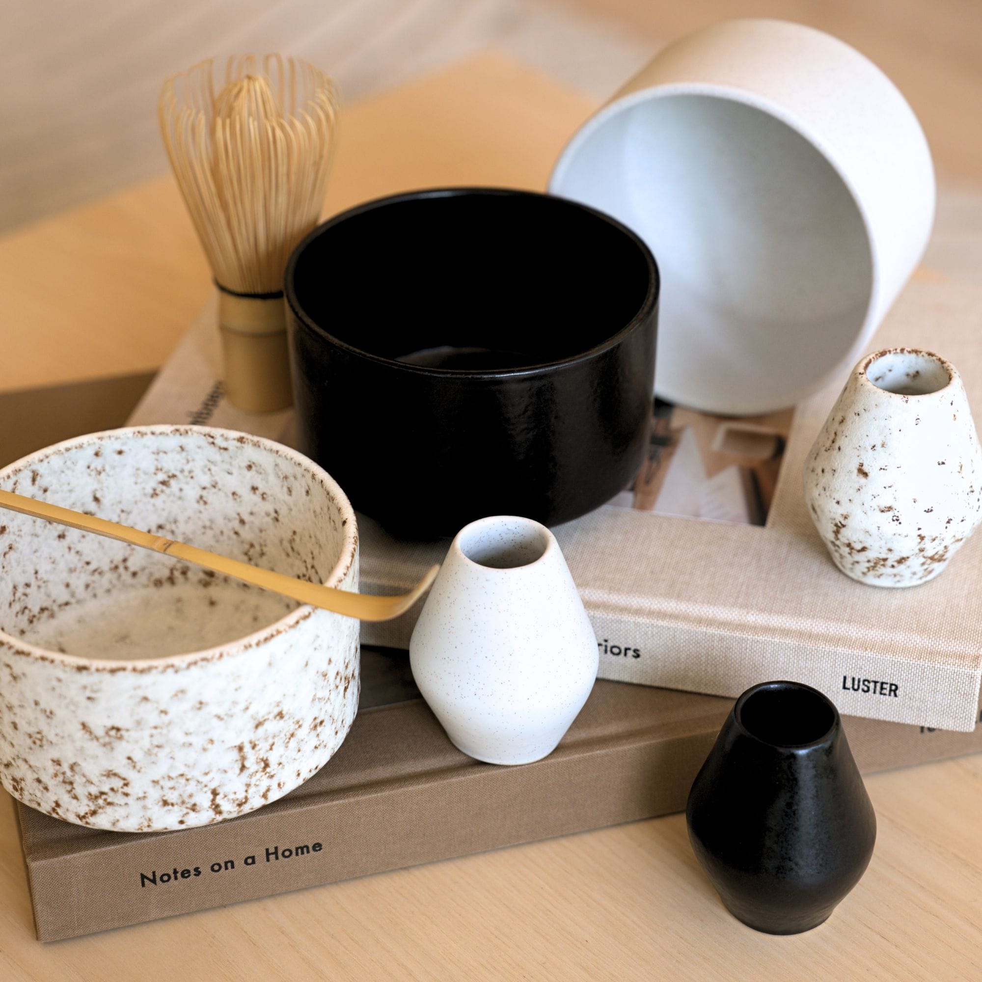 Keramikschalen, Vasen und Bambusbesen auf BĂĽchern, stilvolles Interieur-Arrangement.