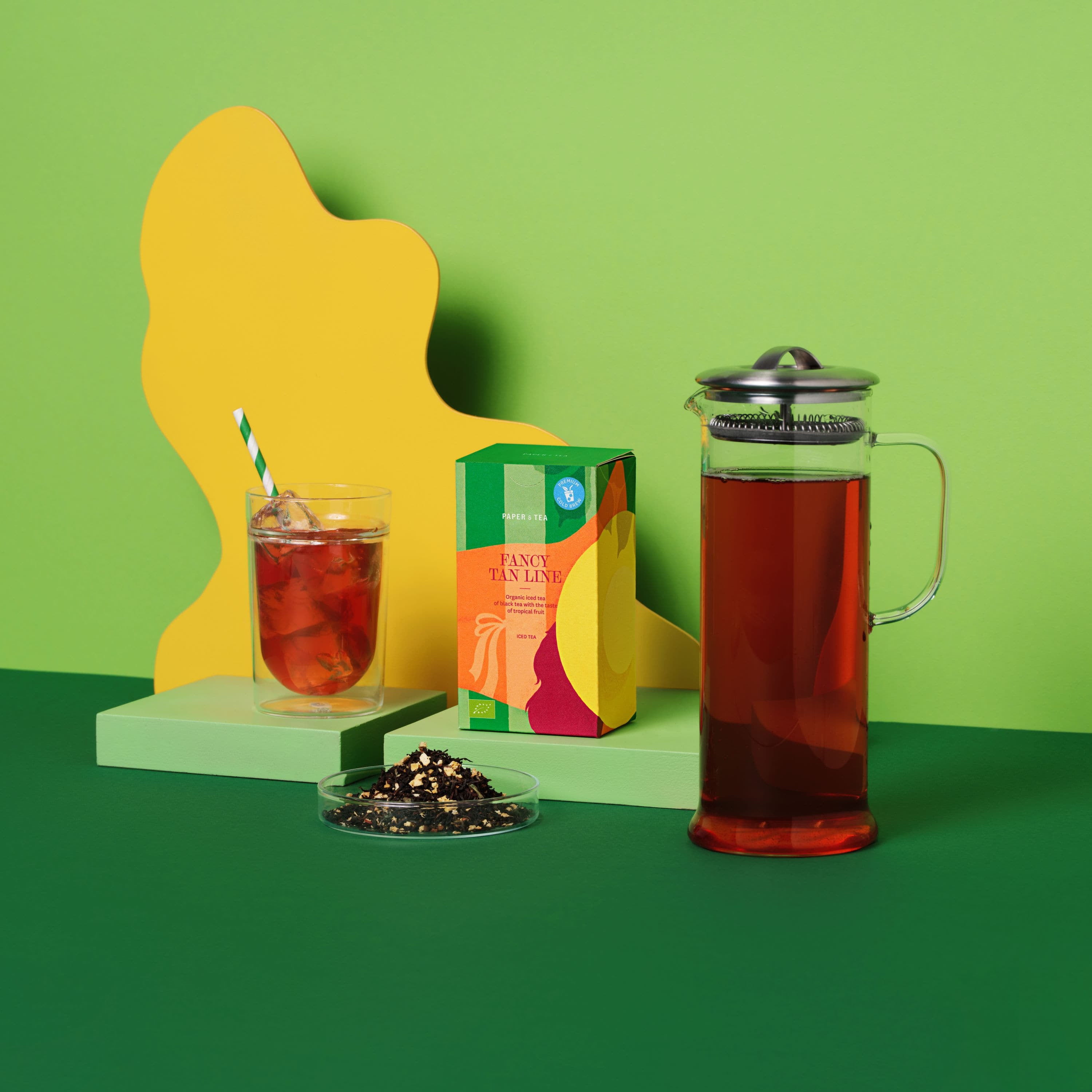 Bunte Verpackung von PAPER & TEA FANCY TAN LINE Bio-Eistee mit Glas, Eis, gestreiftem Strohhalm und French Press