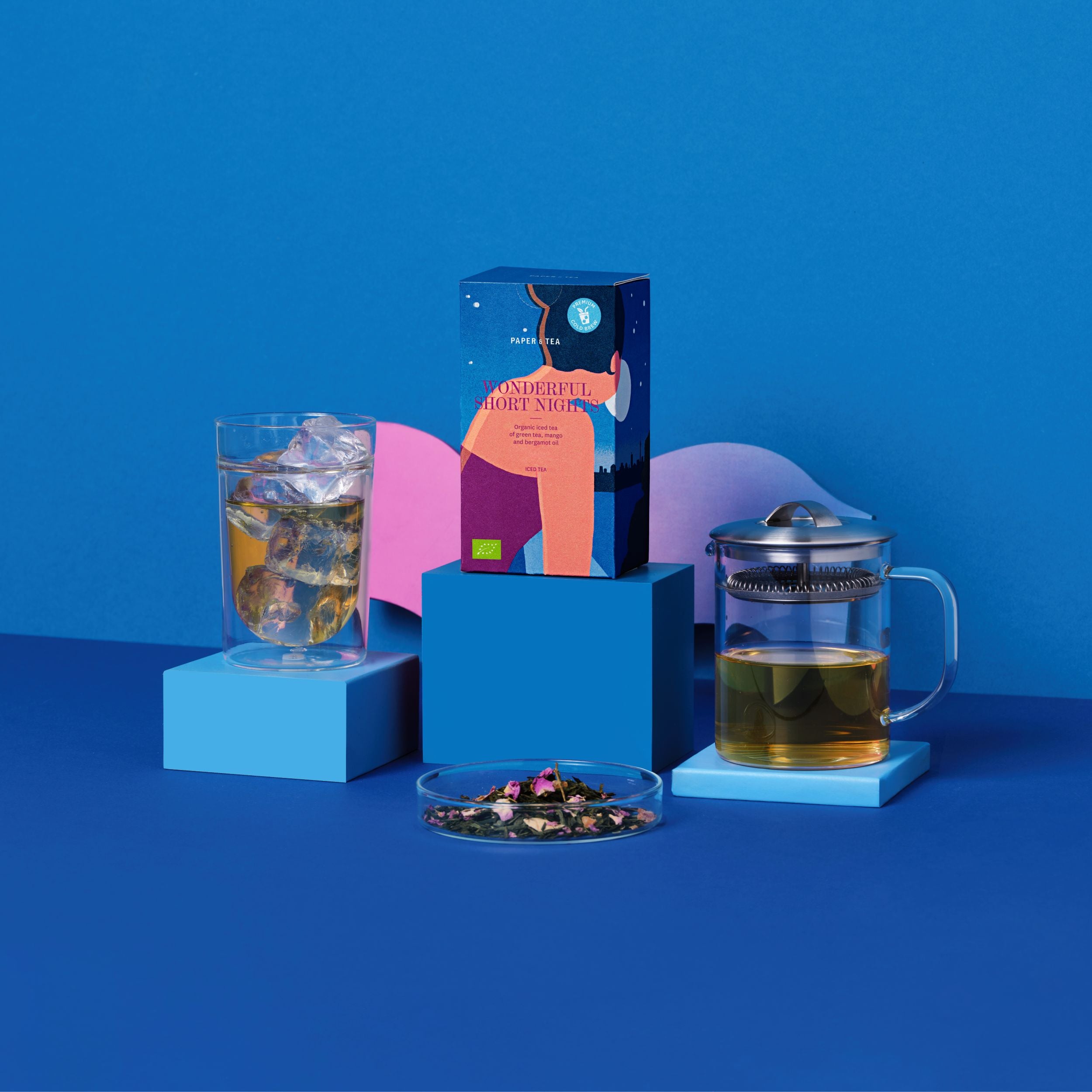 Premium Bio-Eistee 'Wonderful Short Nights' mit grünem Tee, Mango und Bergamotte, neben Glas und Teekanne.