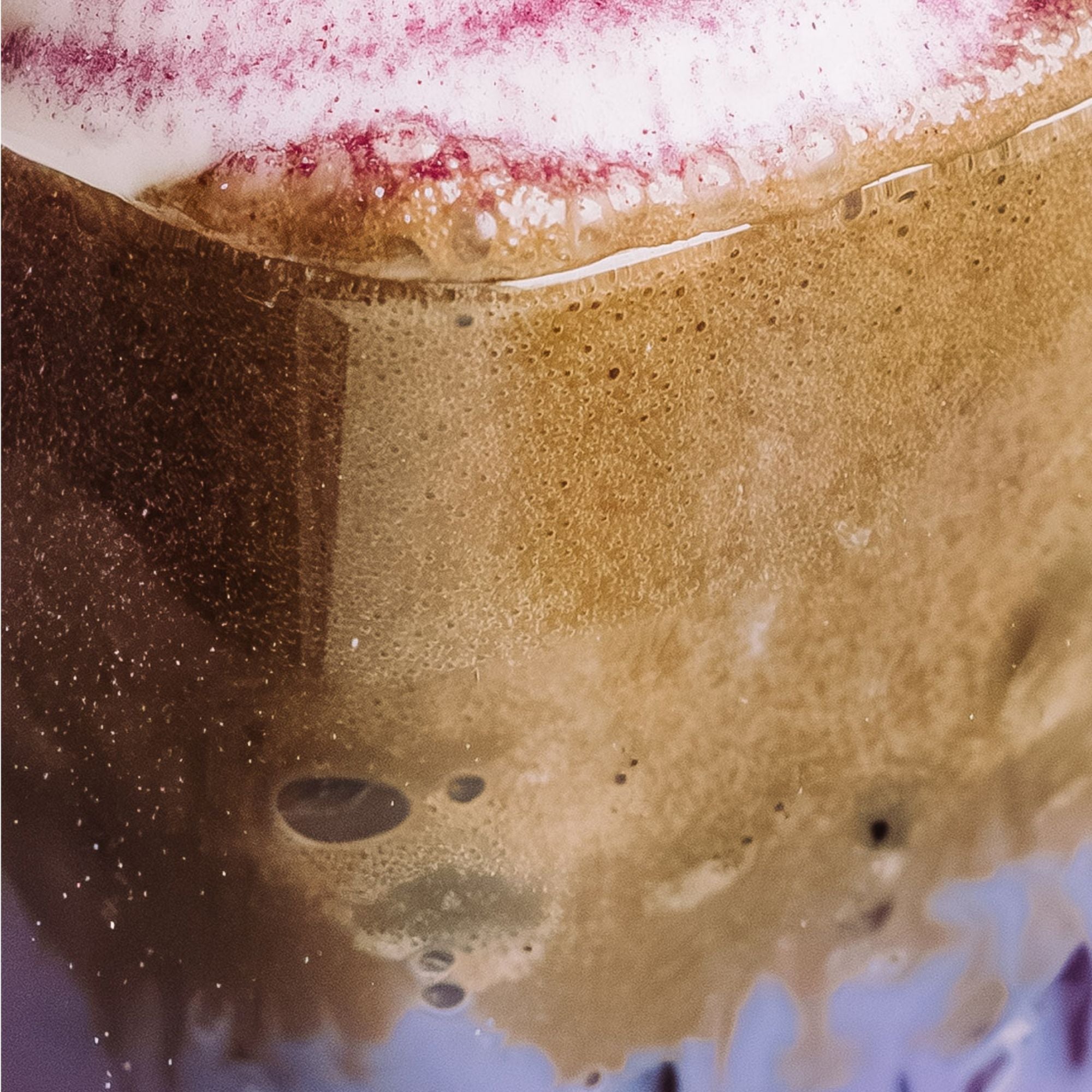 Nahaufnahme eines cremigen Kaffeegetränks mit luftiger Schaumkrone und roten Sprenkeln