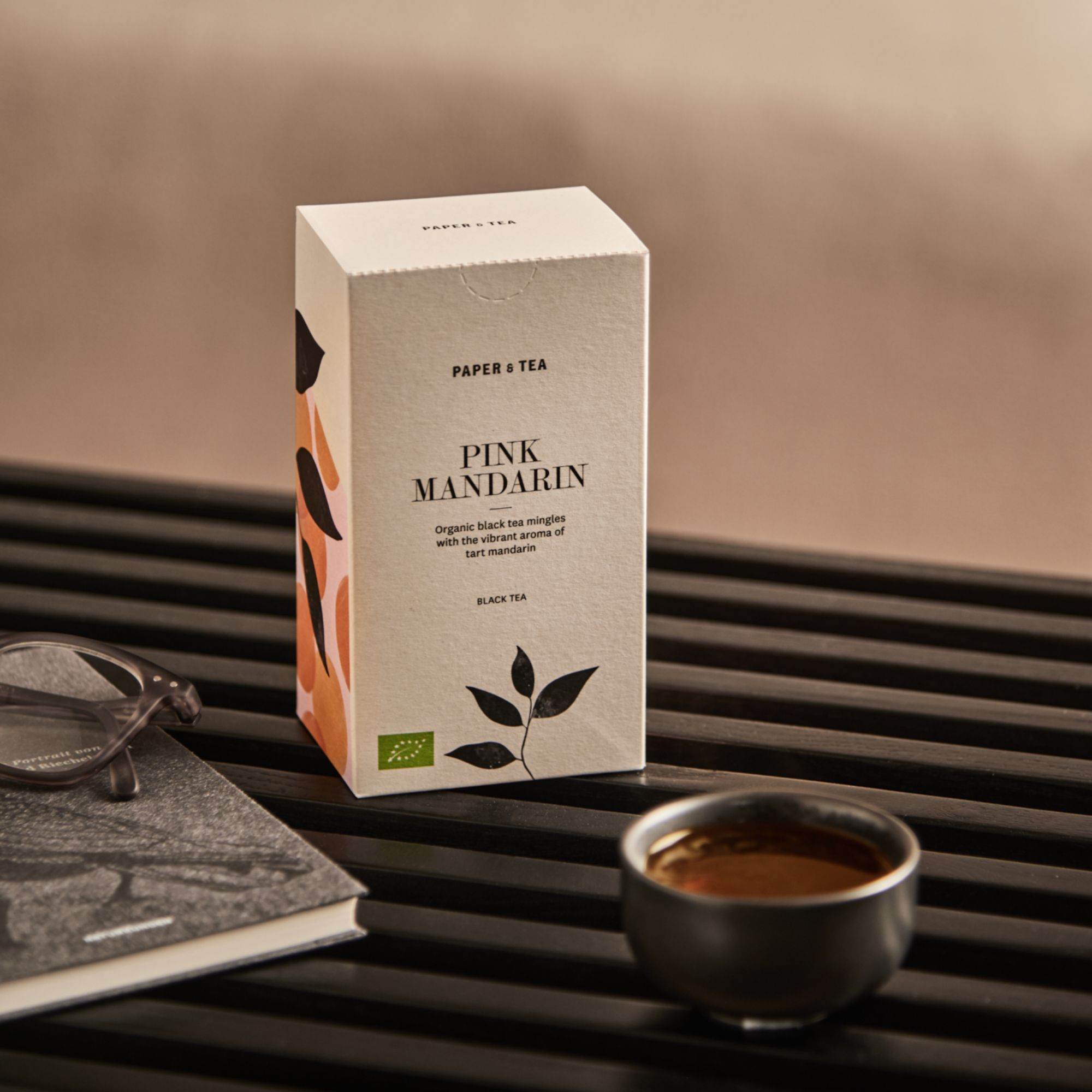 Pale Box mit PAPER & TEA PINK MANDARIN Bio-Schwarztee, Buch, Brille und Teetasse auf Holzbank