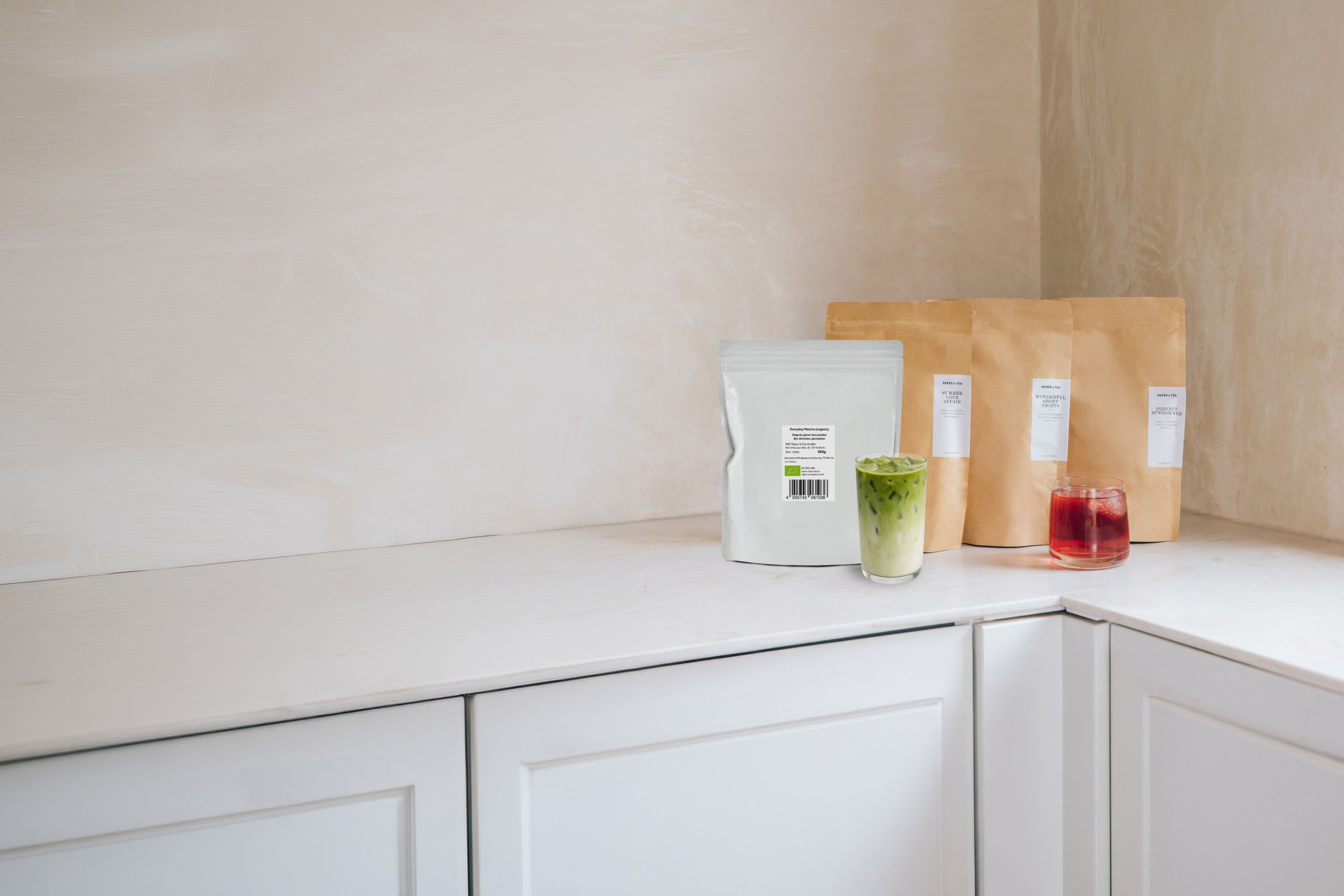 Weißer nachfüllbarer Teebeutel neben Glas Eistee mit Matcha und Milch, P&T Kraftpapier-Teeverpackungen.