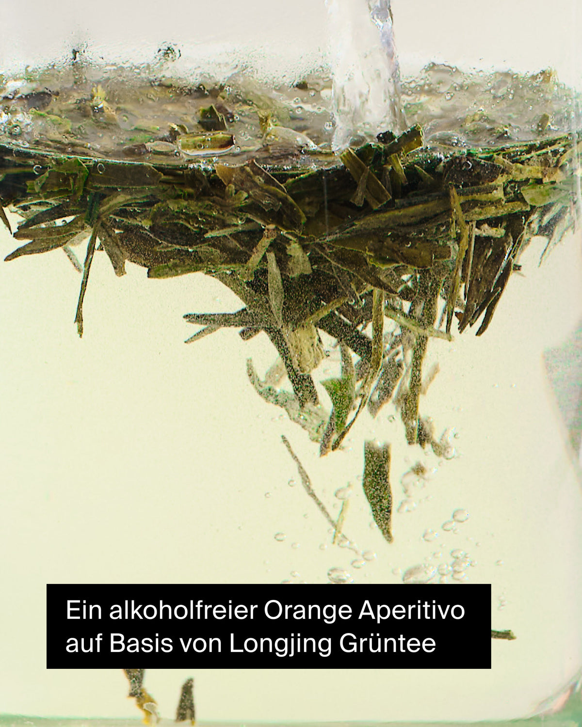 Frische Longjing-Grünteeblätter mit aufsteigenden Bläschen beim Aufgießen für einen Orangen-Aperitivo.