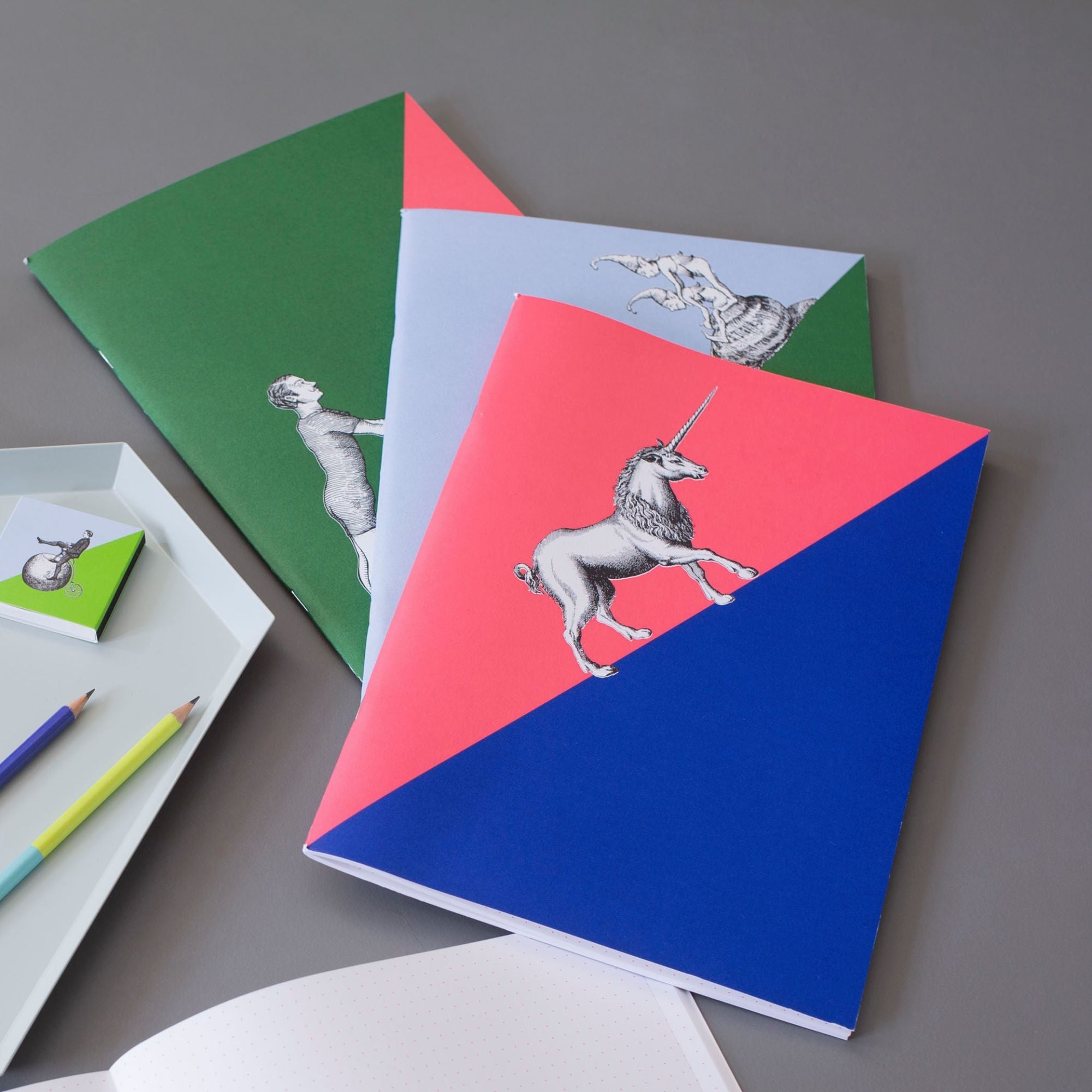 Künstlerische Notizbücher: Einhorn-Motiv auf pink-blauem Einband, Vintage-Designs, Buntstifte, offenes gepunktetes Notizbuch.