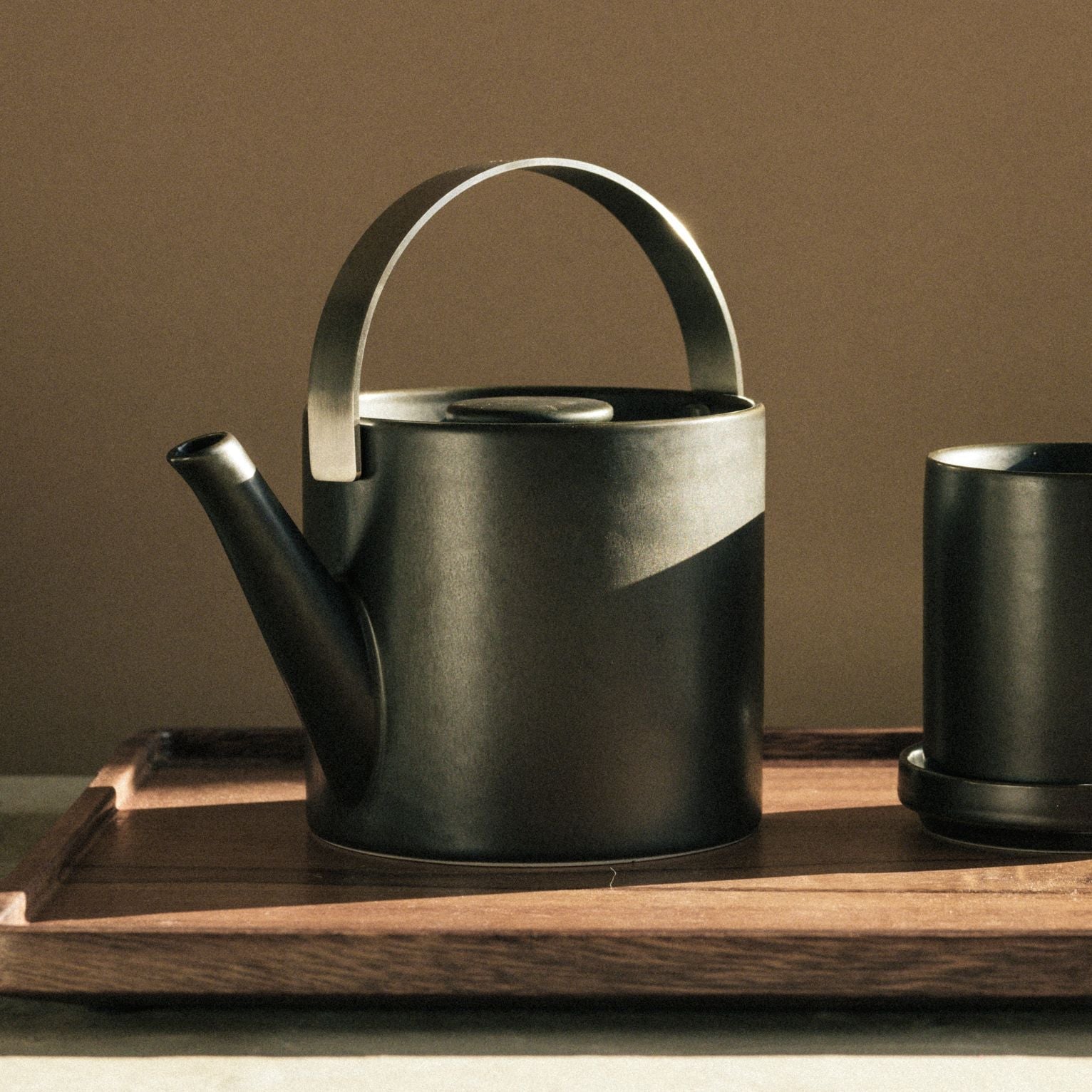 Mattschwarzes Teeset mit schlankem, zylindrischem Teekessel und passender Tasse auf Holztablett.