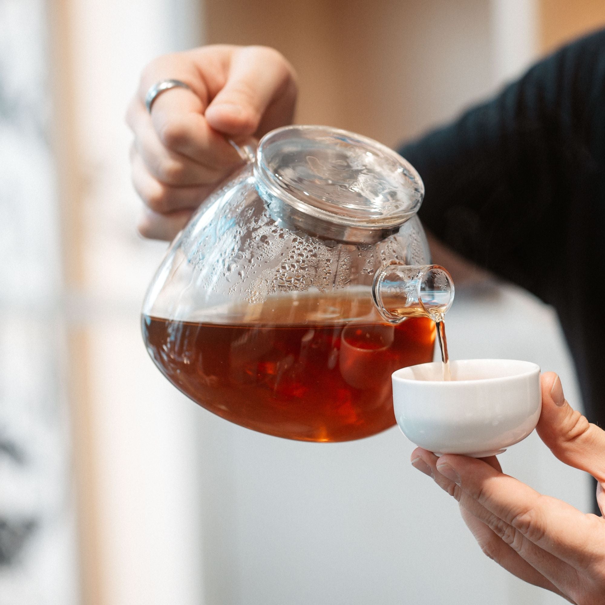 Dunkler Bernsteintee wird aus einem Glas-Teekessel in eine weiße Keramiktasse gegossen.