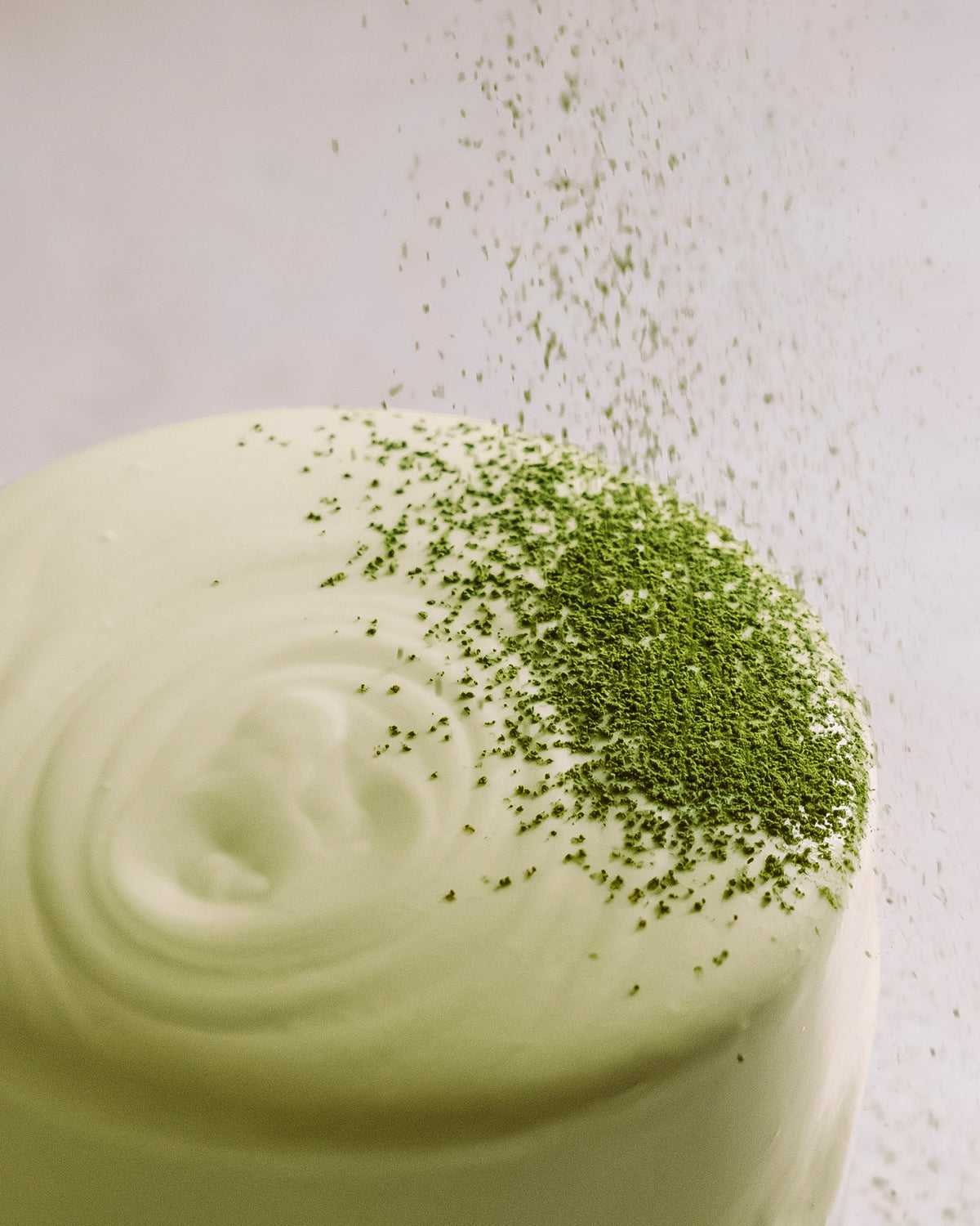 Weiße Keramiktasse mit cremigem Milchschaum und grünem Matcha-Pulver, sanft darüber gestreut.