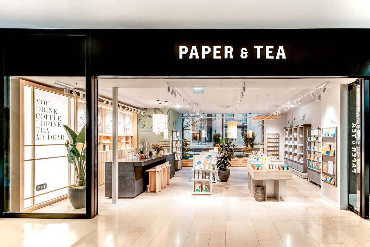 Moderner Eingang von PAPER & TEA mit beleuchtetem Frühstücks-Tee-Podium und Pflanzenakzenten.