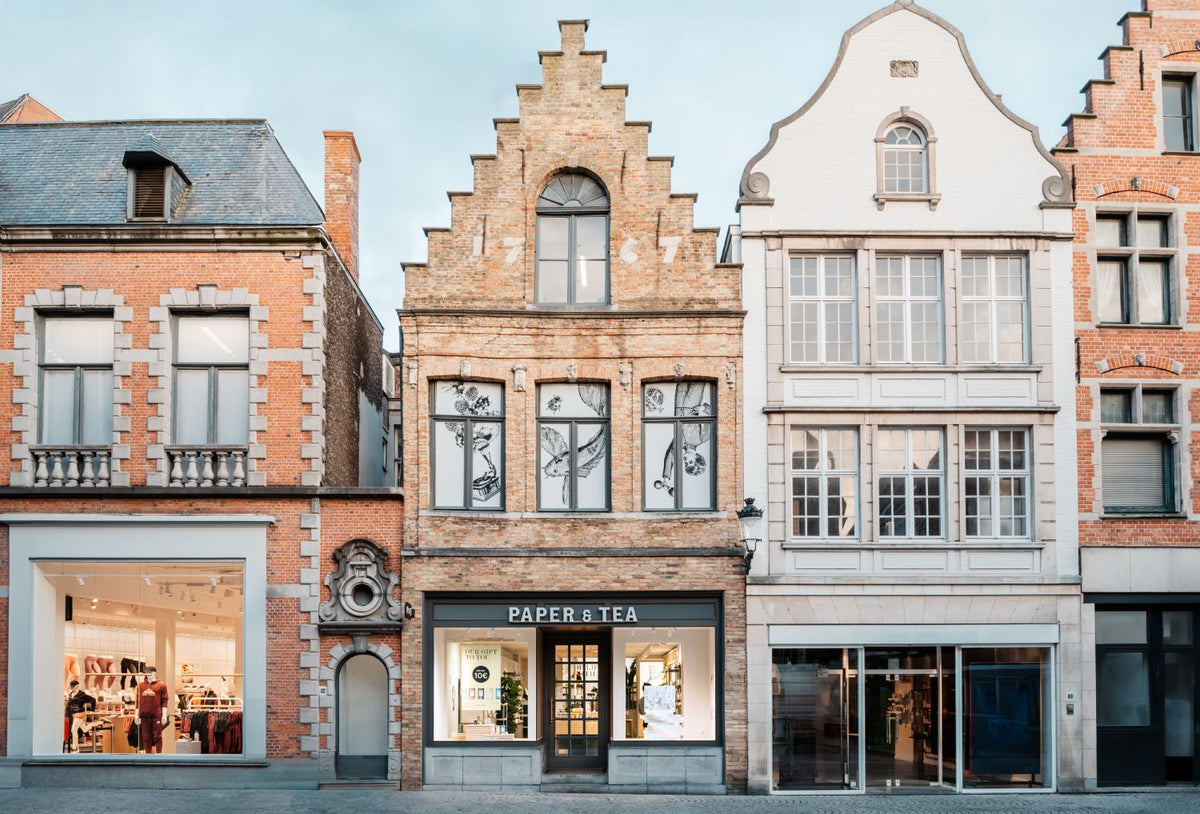 Historisches europäisches Gebäude mit 'PAPER & TEA' Shop in Ziegelfassade an Kopfsteinpflasterstraße.