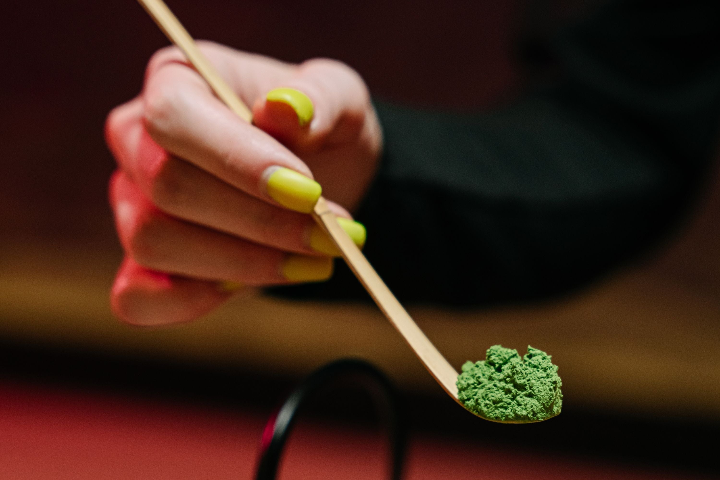 Hand mit Nagellack hält einen kleinen Holzlöffel mit feinem Matcha-Pulver
