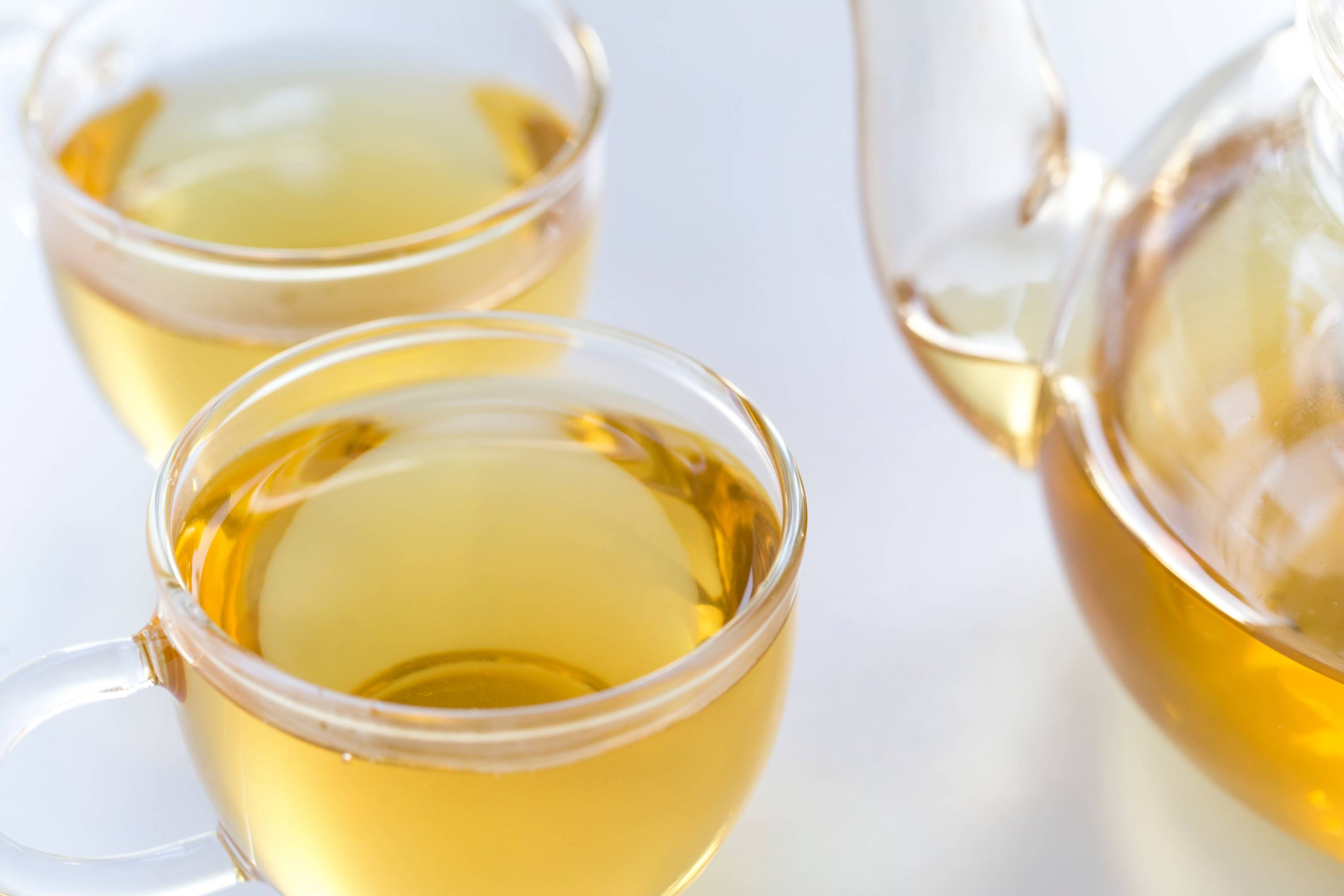 Zwei transparente Gläser mit hellgelbem Tee neben einem Glas-Teekännchen auf Tisch
