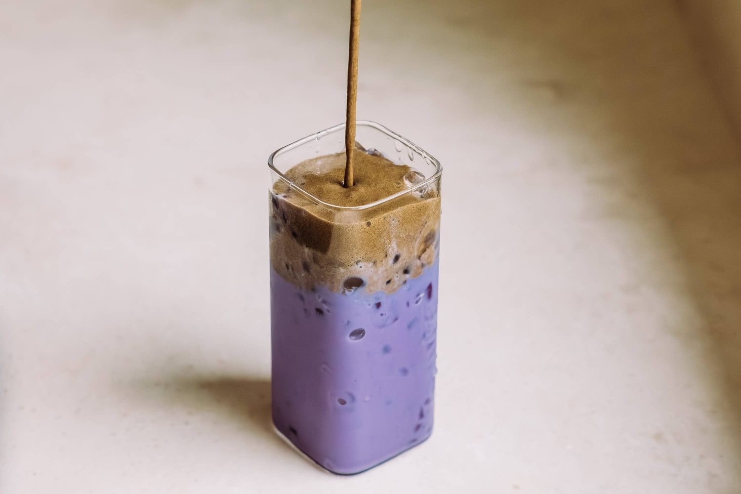 Iced Latte in Glas mit violetter Ube-Schicht und schaumiger Hojicha-Schicht.