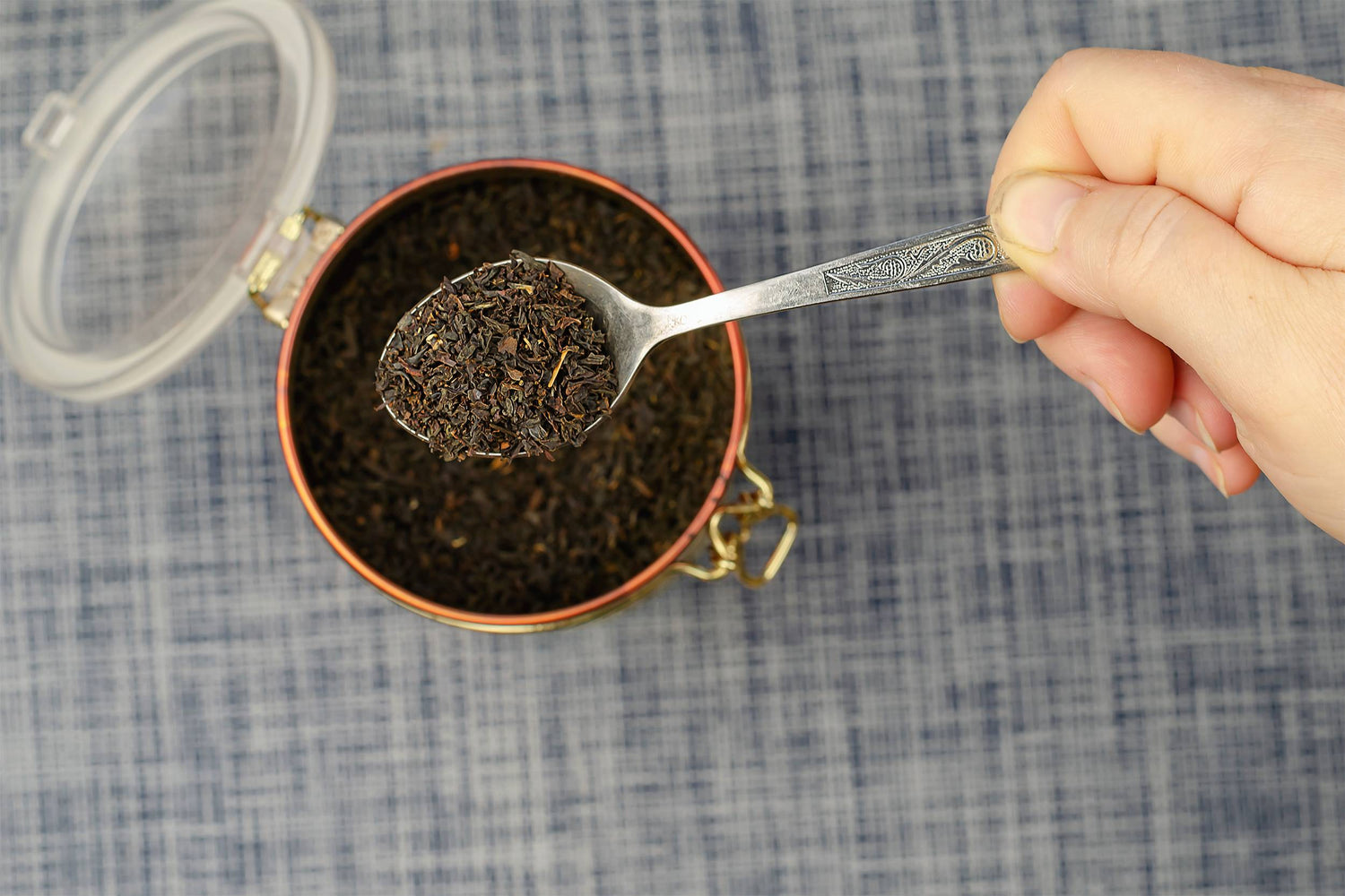 Silberner Löffel mit losen schwarzen Teeblättern über geöffneter Teedose