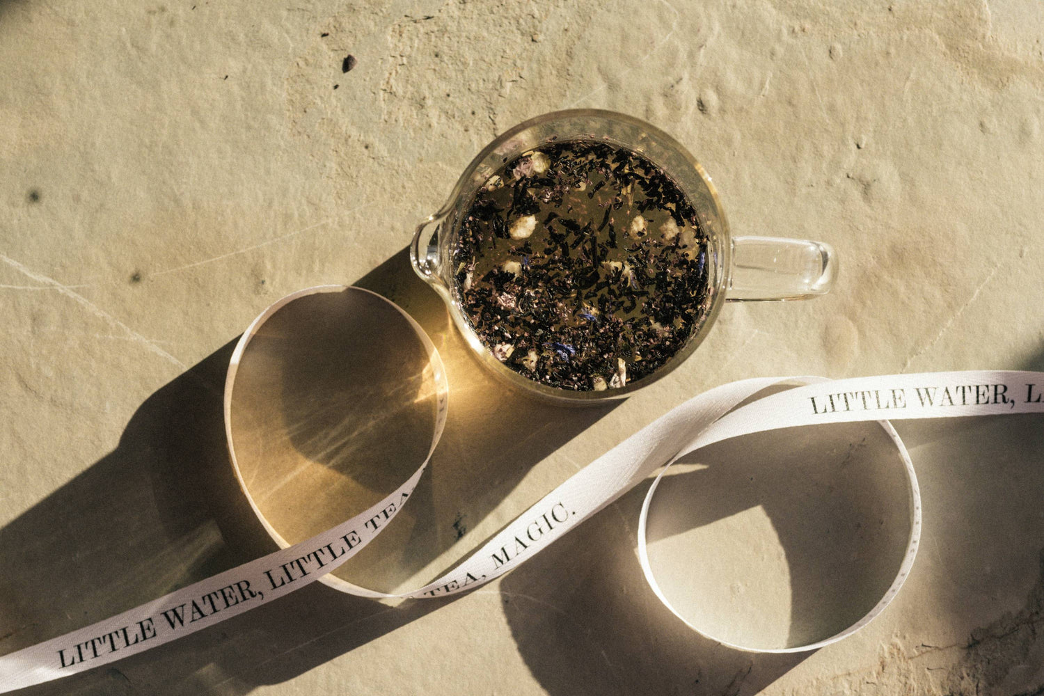 Glasbecher mit Tee und schwebenden Teeblättern, umgeben von Band