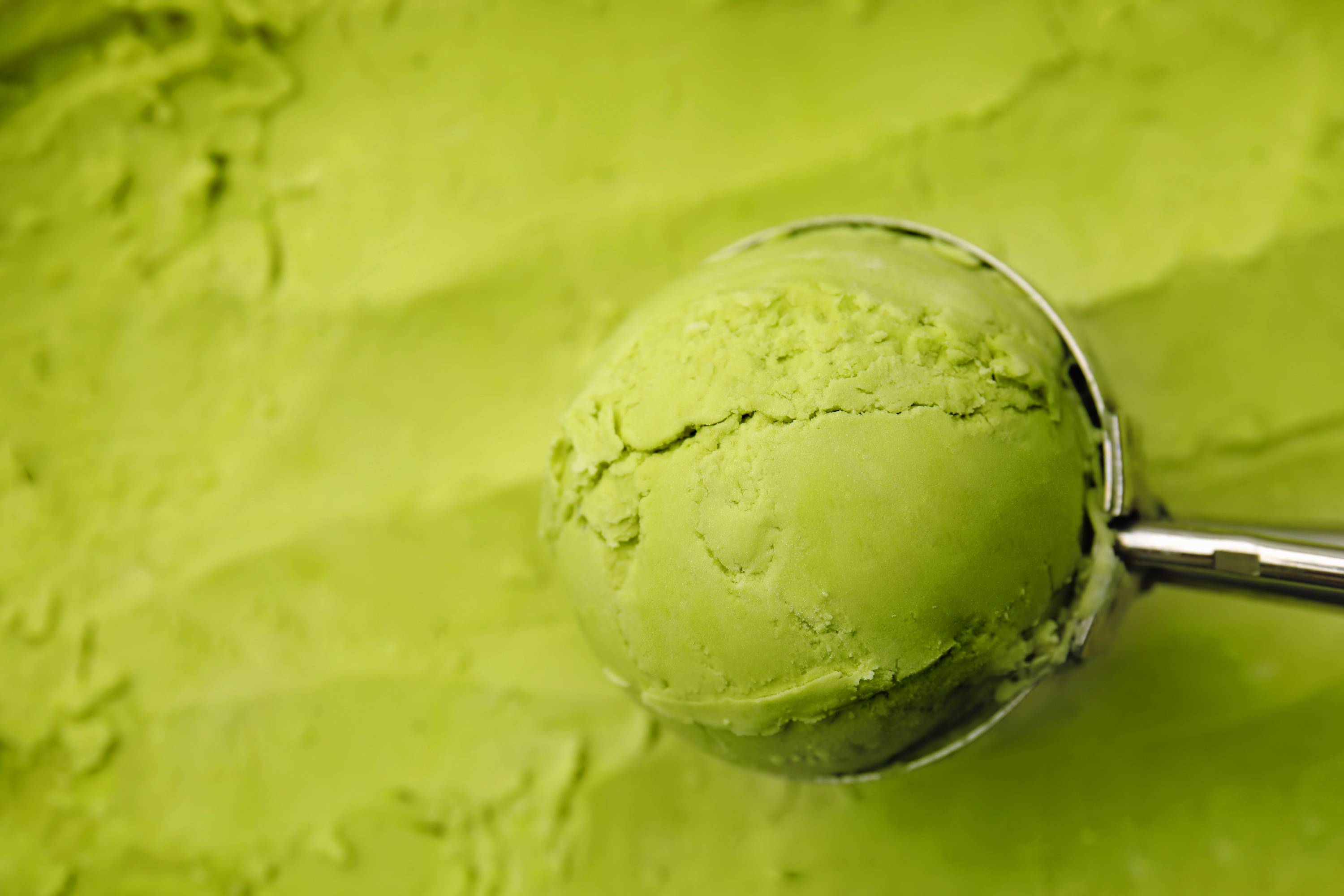 Eiskugelportionierer mit grünem Matcha-Eis vor Eis im Hintergrund