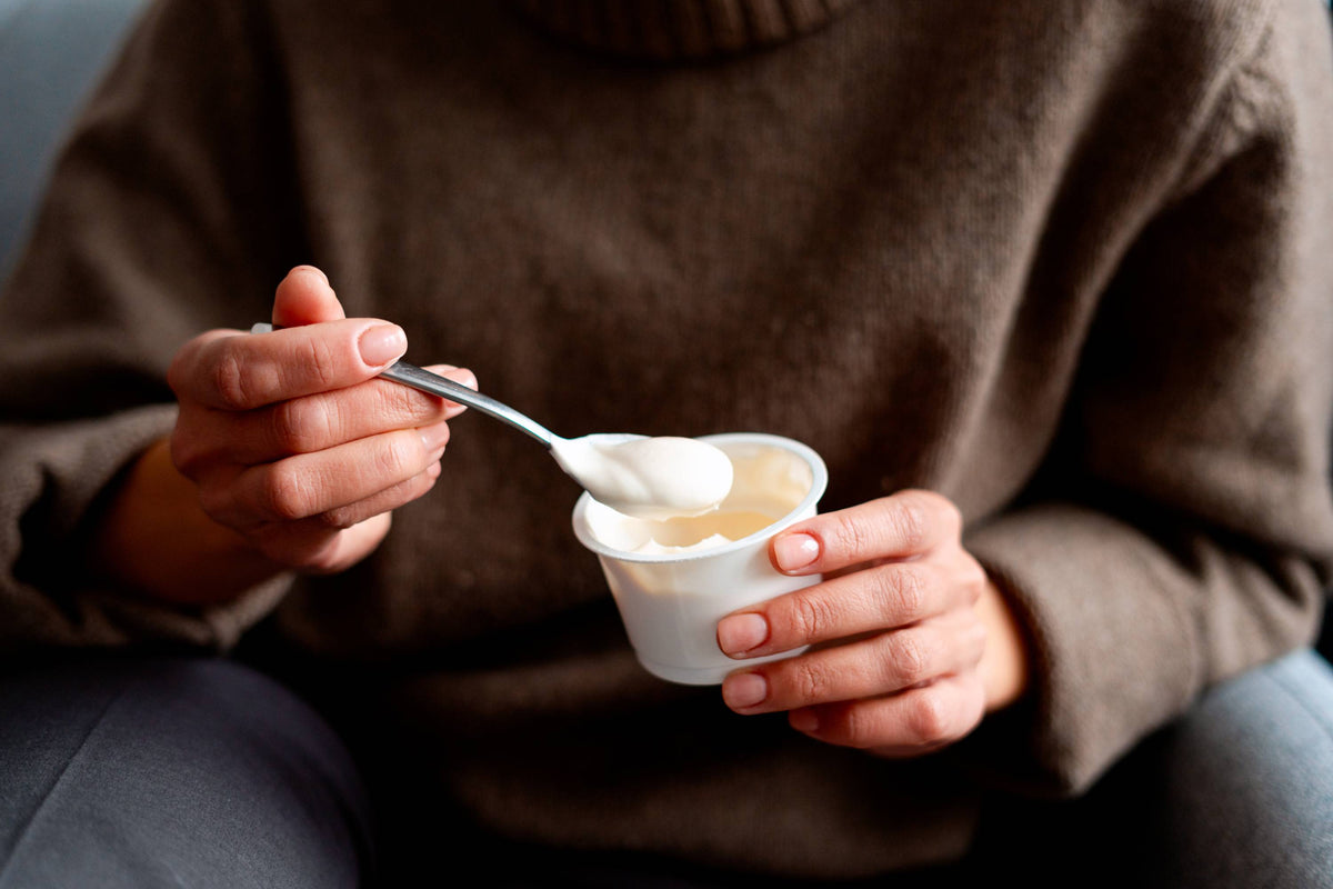 Person in braunem Pullover hält Becher mit cremigem Joghurt