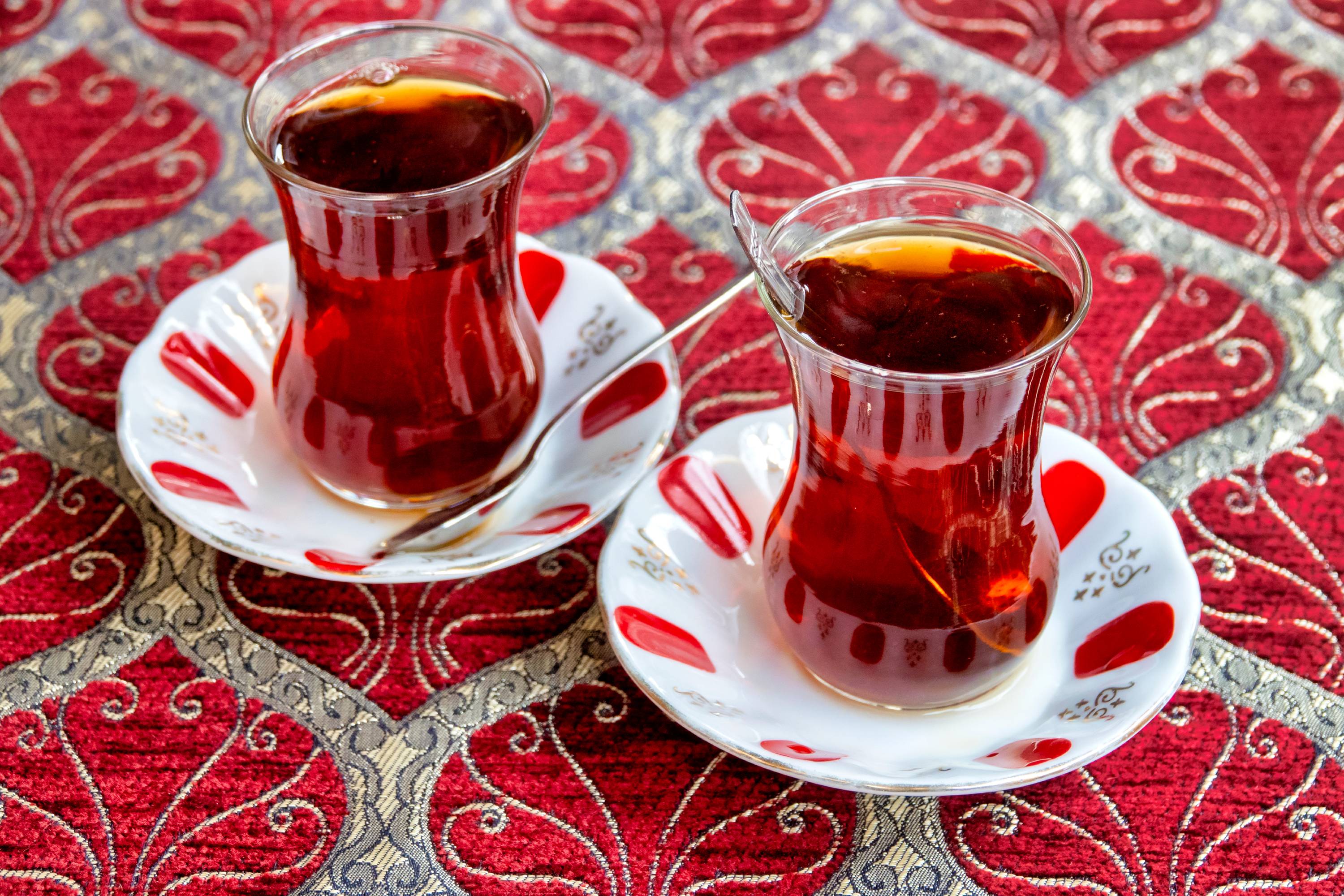 Traditionelle türkische Teegläser mit schwarzem Tee auf verzierten Untertassen auf rotem Tischläufer
