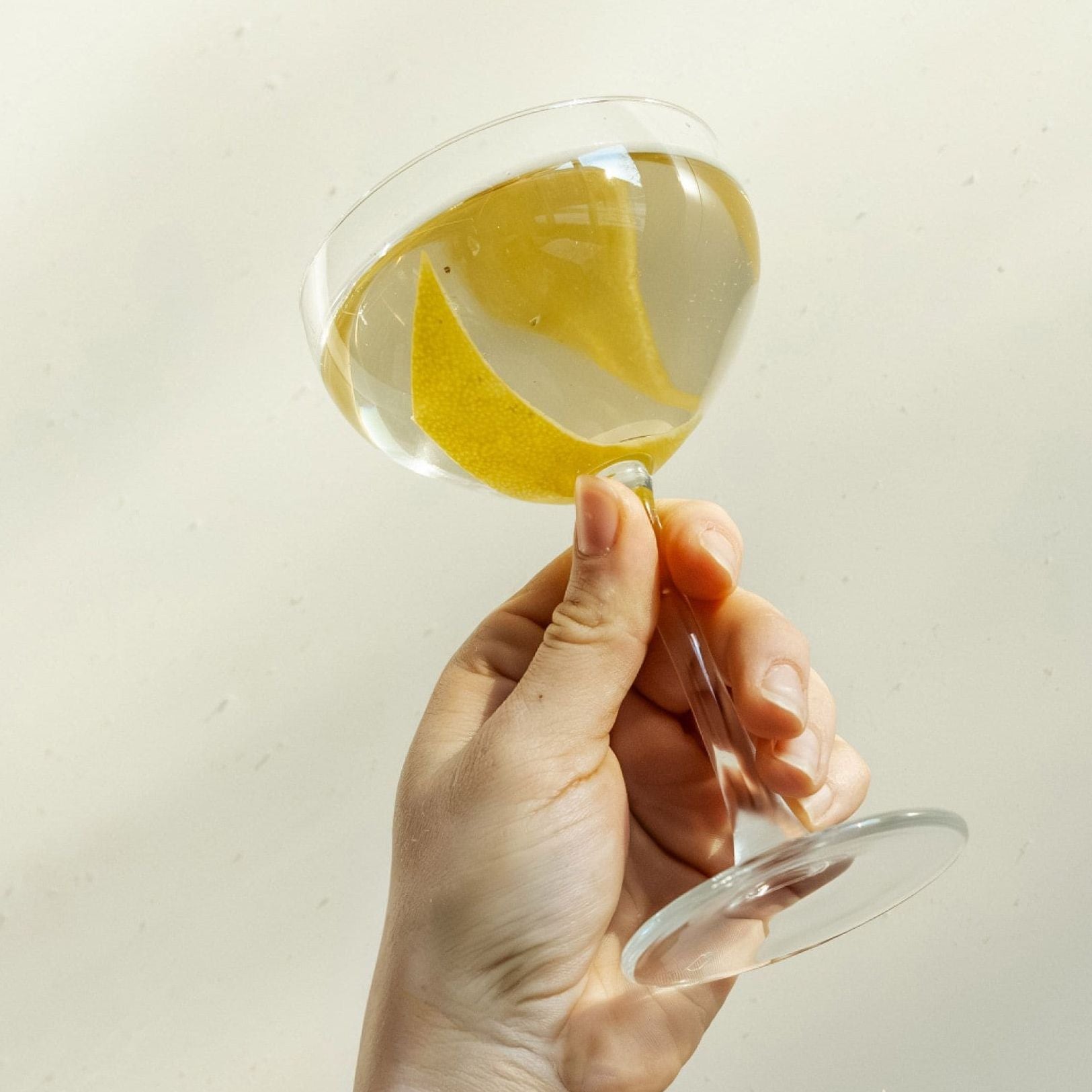 Hand hält ein elegantes Cocktailglas mit klarem Getränk und Zitronenschale als Garnitur.