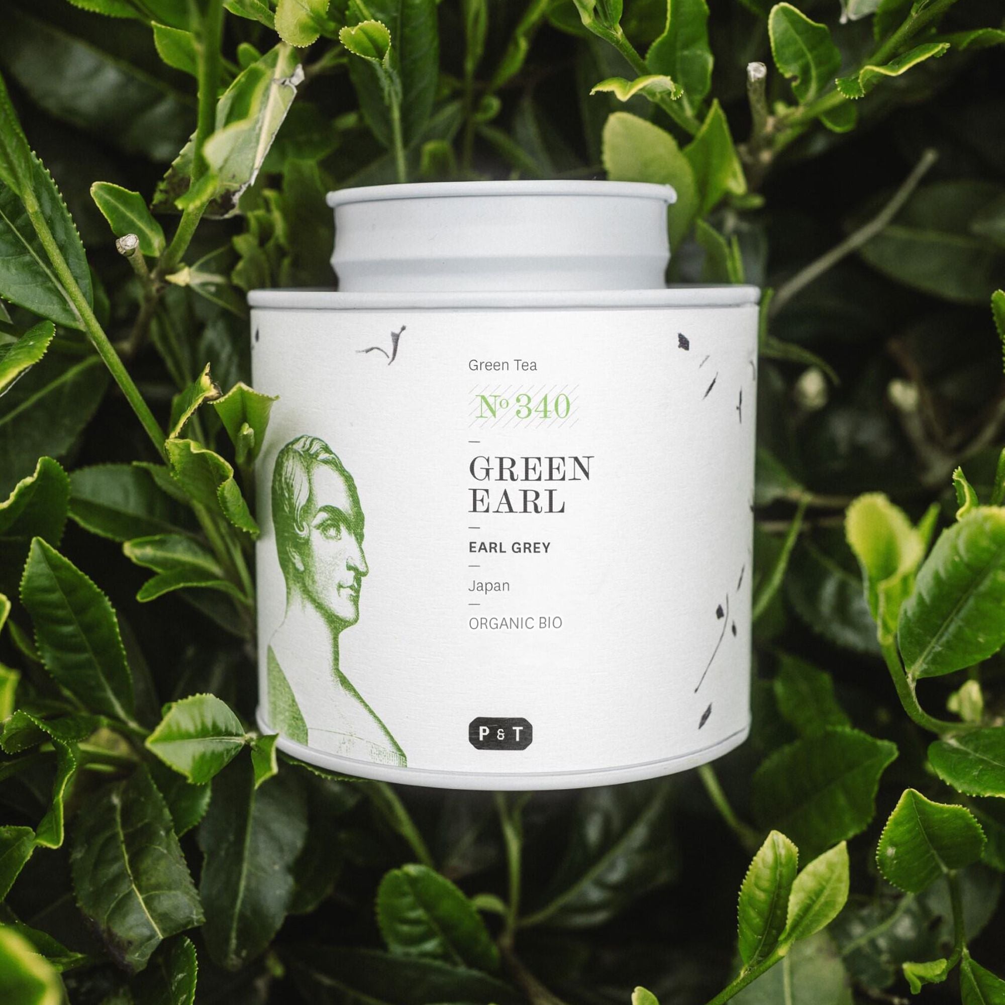 Weißer Teebehälter mit grünem Männerprofil und 'Green Earl'-Beschriftung, umgeben von grünen Teeblättern.