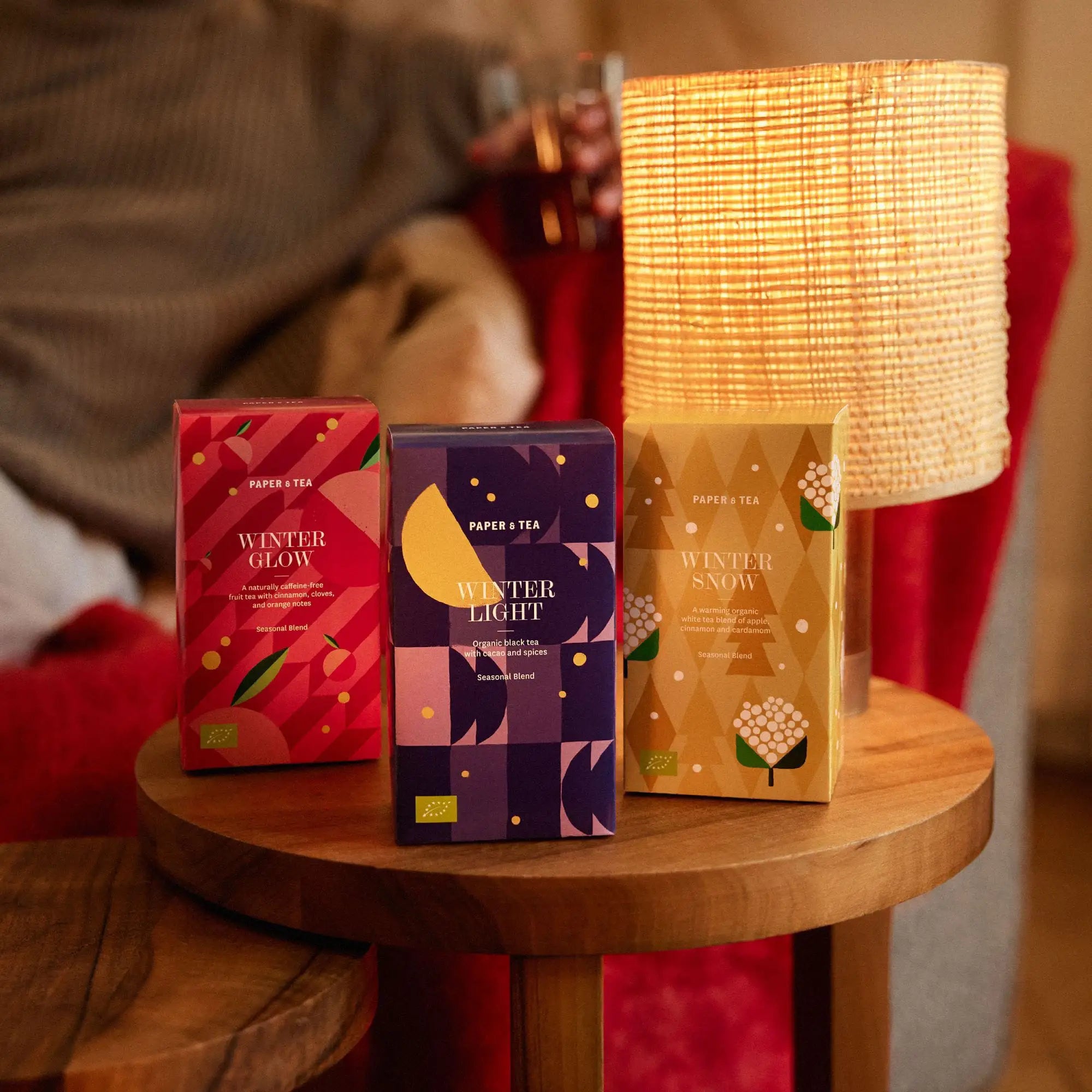 Drei farbenfrohe PAPER & TEA Winter-Teeboxen mit Glühwein-, Schwarztee- und Weißtee-Mischungen auf Holztisch.