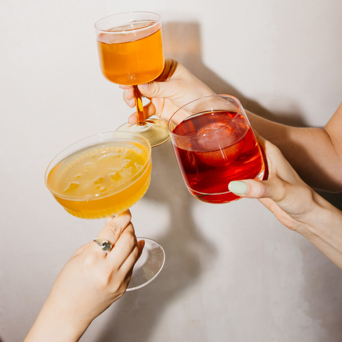 Drei Hände mit verschiedenen Cocktails in stilvollen Gläsern, symbolisieren Genuss und Geselligkeit.