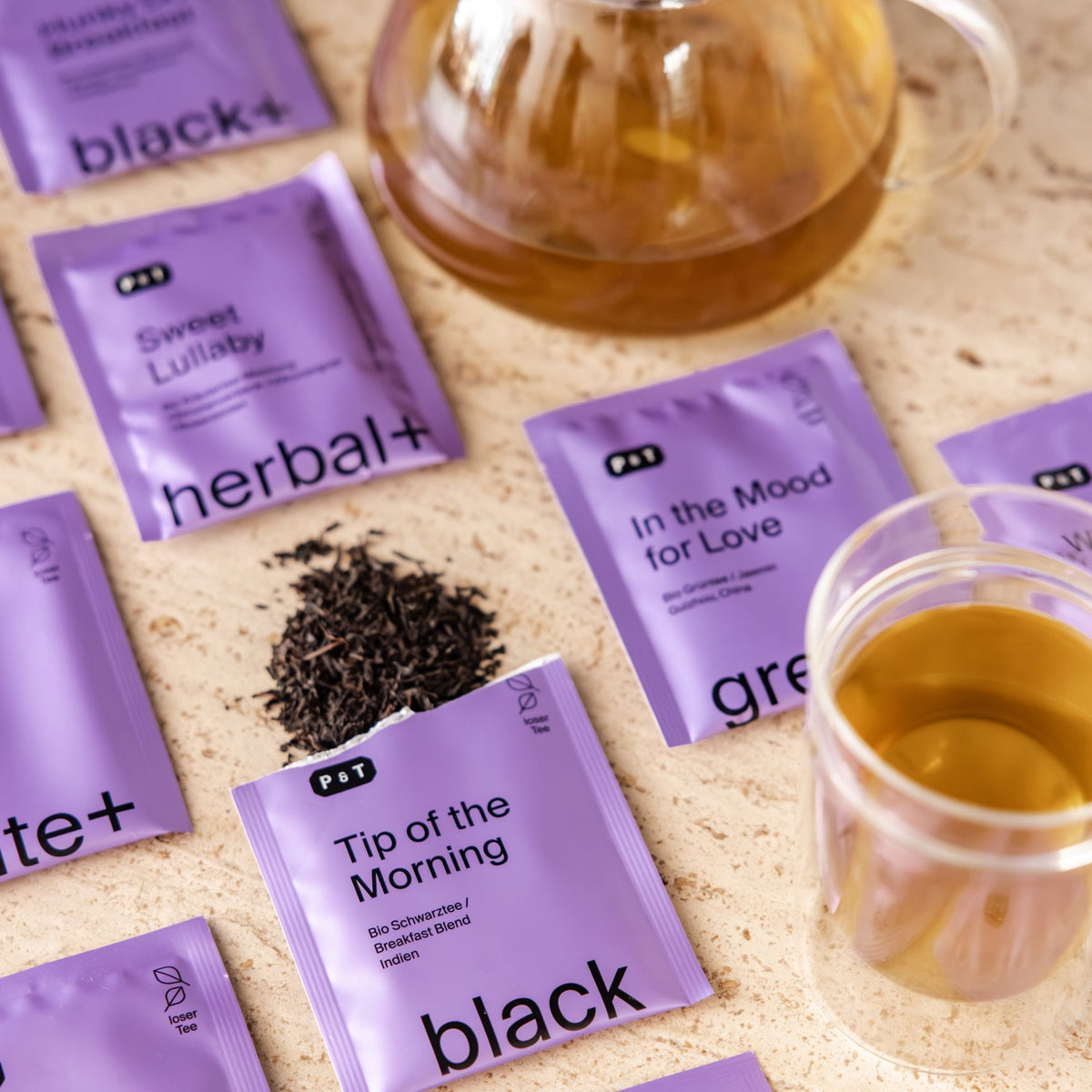Violette P&T Teepackungen mit Sorten Sweet Lullaby und Tip of the Morning, dazu losen Schwarztee, Teekanne und Teetasse.