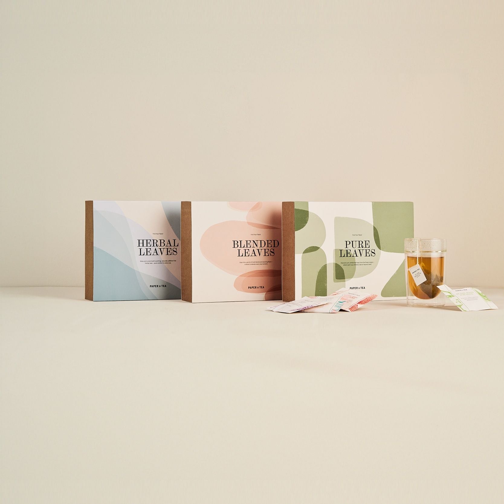 Drei rechteckige Tee-Boxen mit Herbal, Blended und Pure Leaves, bunte Teebeutel, Glastasse mit Tee.