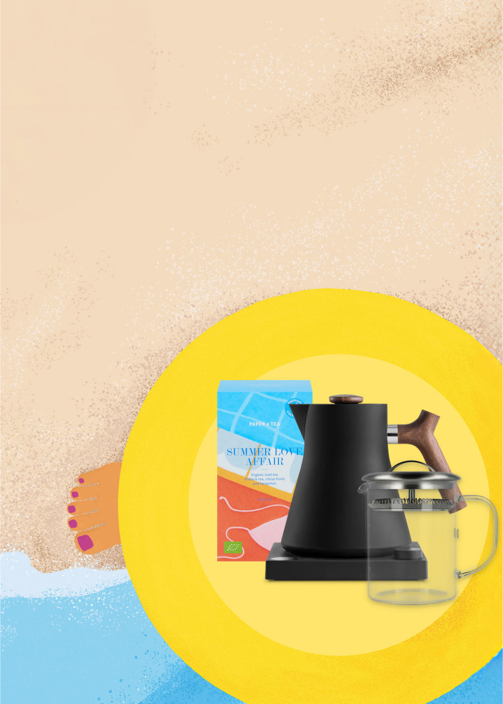 Bunte Verpackung von Paper & Tea Summer Love Affair Bio-Eistee neben schwarzem Wasserkocher und Glas-Teekanne auf gelber Strandmatte im Sand.