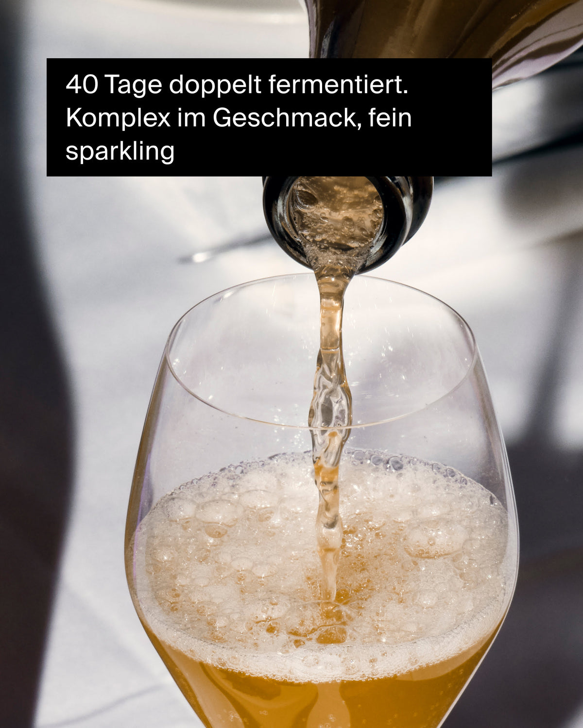 Ein Glas wird mit einem goldenen, fein sprudelnden Getränk aus einer Flasche gefüllt. Doppelter Gärungsvorgang über 40 Tage.