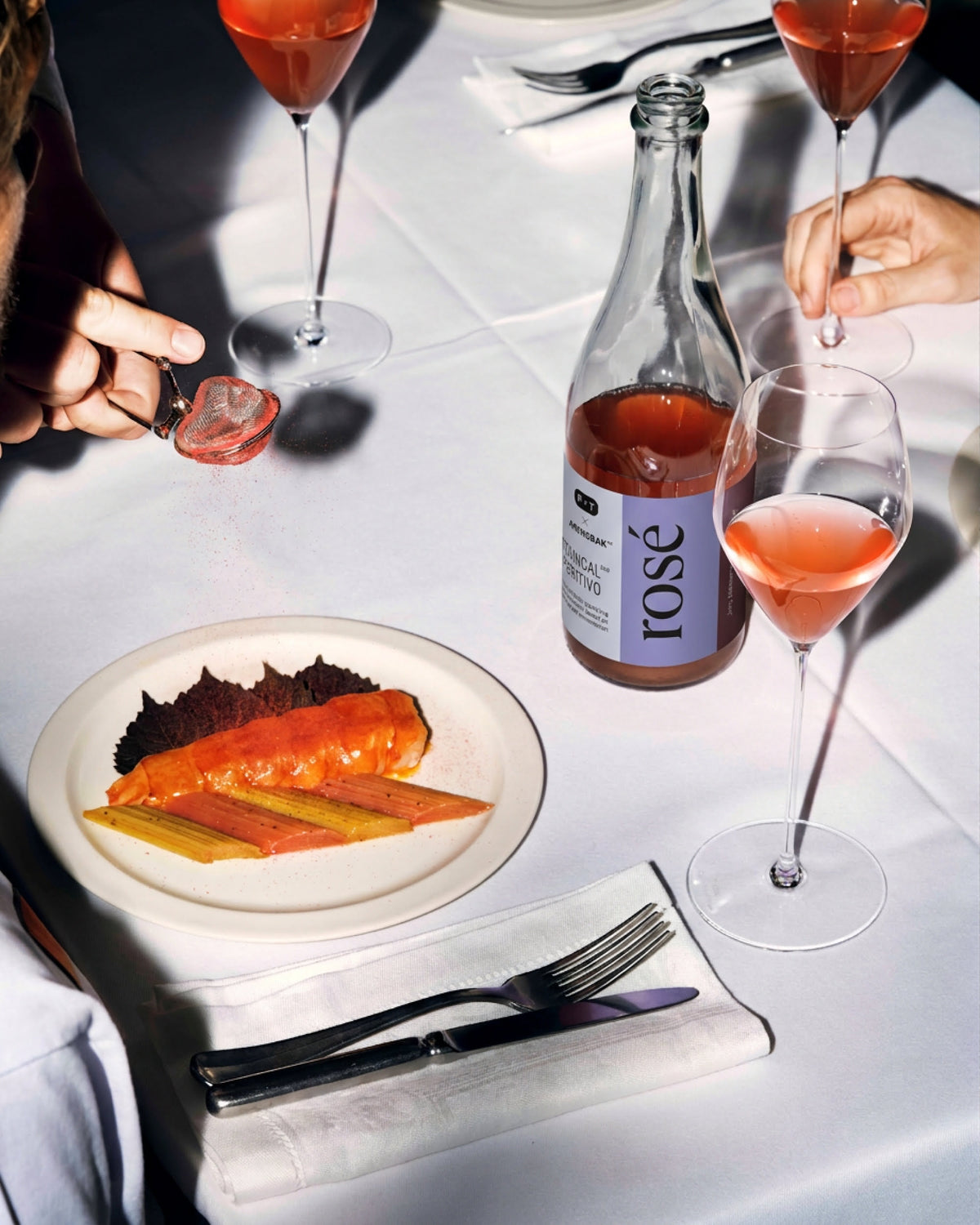 Elegante Tischszene mit Roséwein, drei gefüllten Gläsern und einem Teller mit Gemüse.