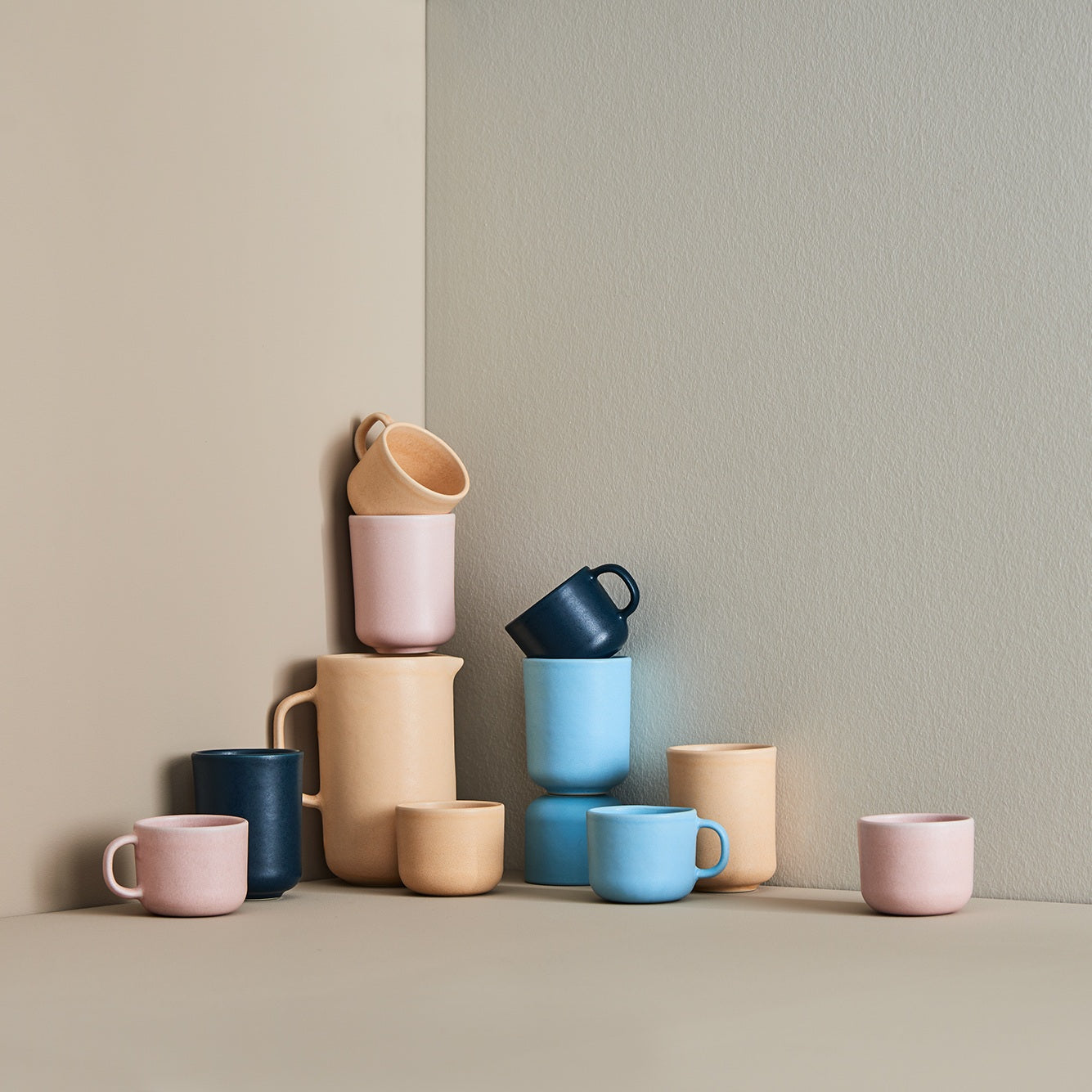 Keramikbecher und Krug in Pastellfarben vor beigen Wänden, von Iittala.