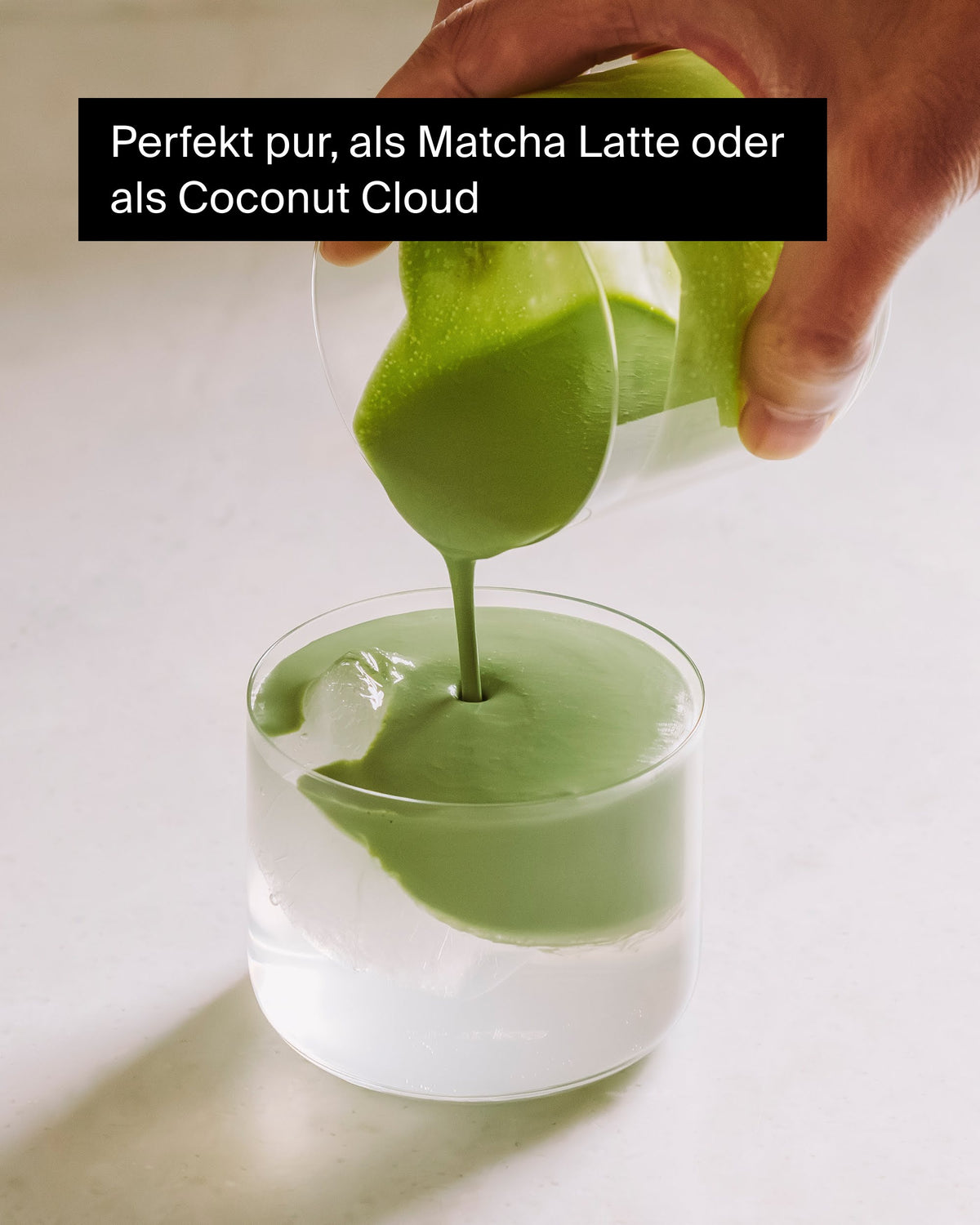 Hand gießt cremigen grünen Matcha in ein Glas mit Eiswürfeln für Matcha Latte.