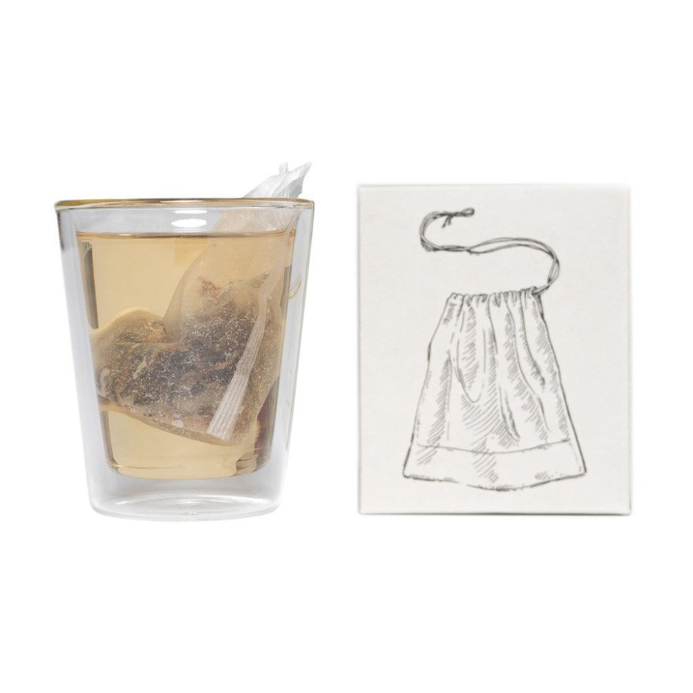Klarer Glasbecher mit hellem braunem Tee und zwei Teebeuteln, neben einem weißen Karton mit Teebeutel-Symbol.