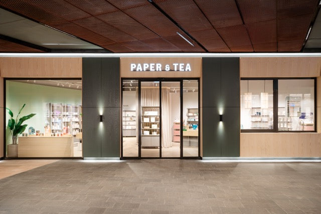 Moderne P&T Ladenfront mit beleuchtetem Schild, großen Glastüren, Holzregalen und Innenpflanze