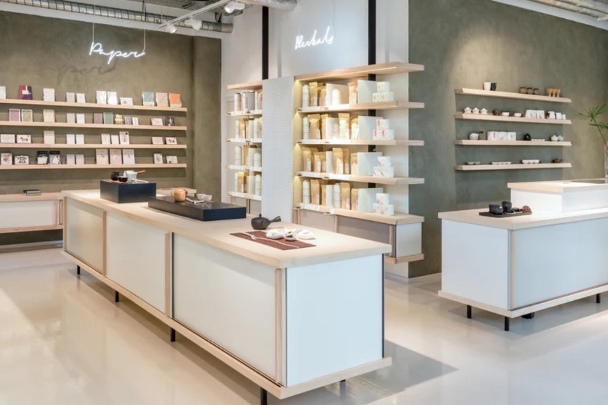 Ein moderner, minimalistischer Laden mit weißen Vitrinen und Holzregalen, die Teekannen, Tassen und Teeprodukte zeigen.