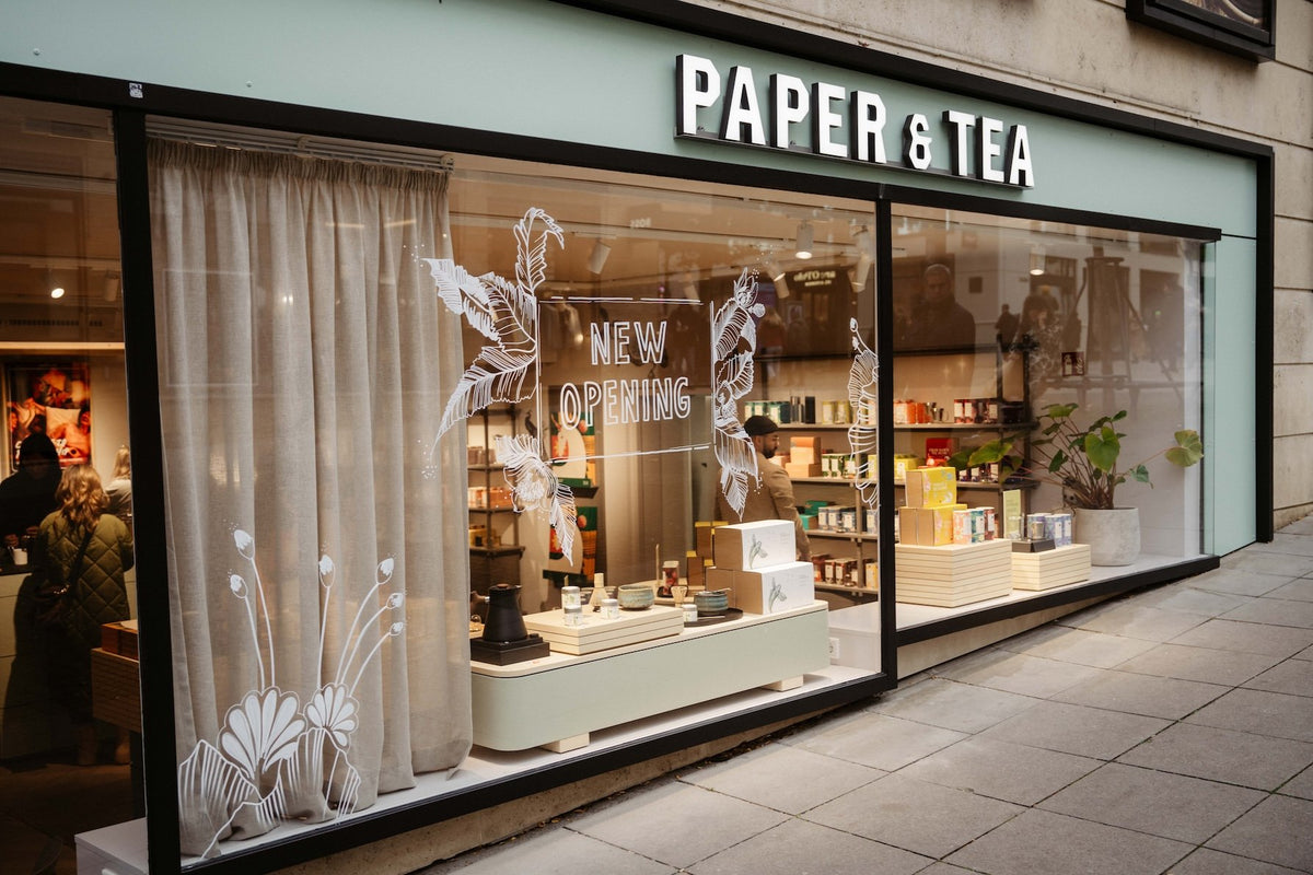 PAPER & TEA Schaufenster mit floraler Dekoration und Holztheke mit verschiedenen Teesorten