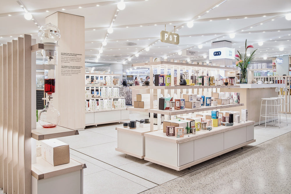 Heller, moderner Teeladen mit P&T-Produkten auf Holzregalen und beleuchtetem P&T-Logo über Verkaufstresen