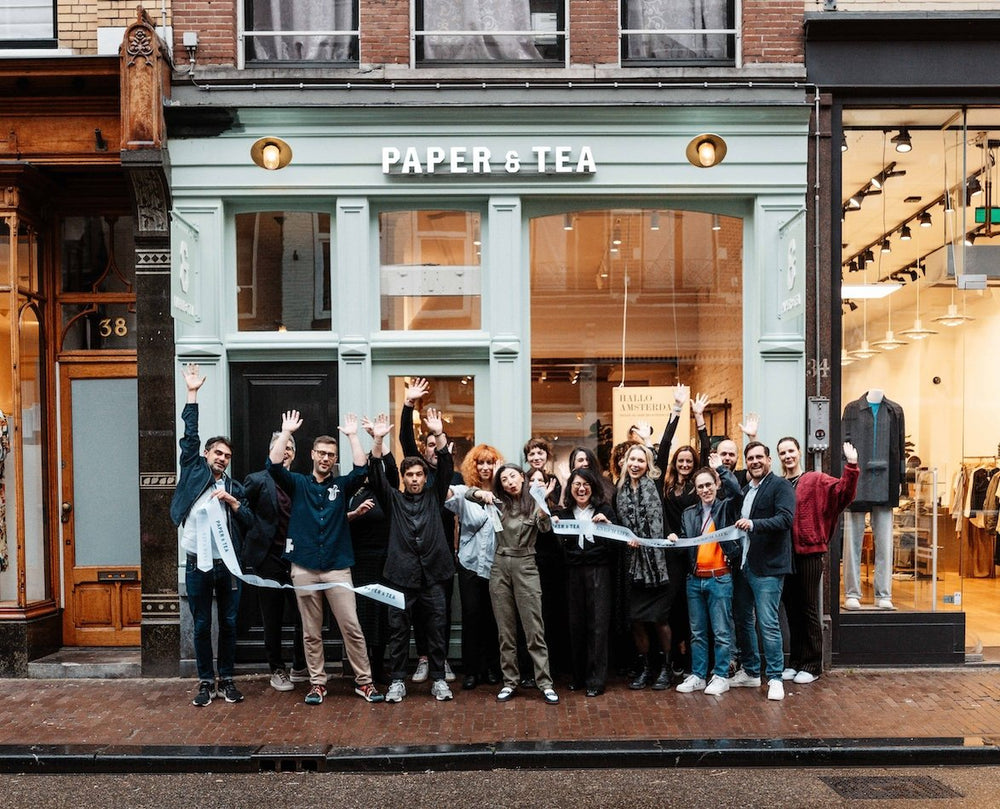 Menschen feiern die Eröffnung des Paper & Tea Ladens mit grüner Fassade und großen Fenstern in Amsterdam.
