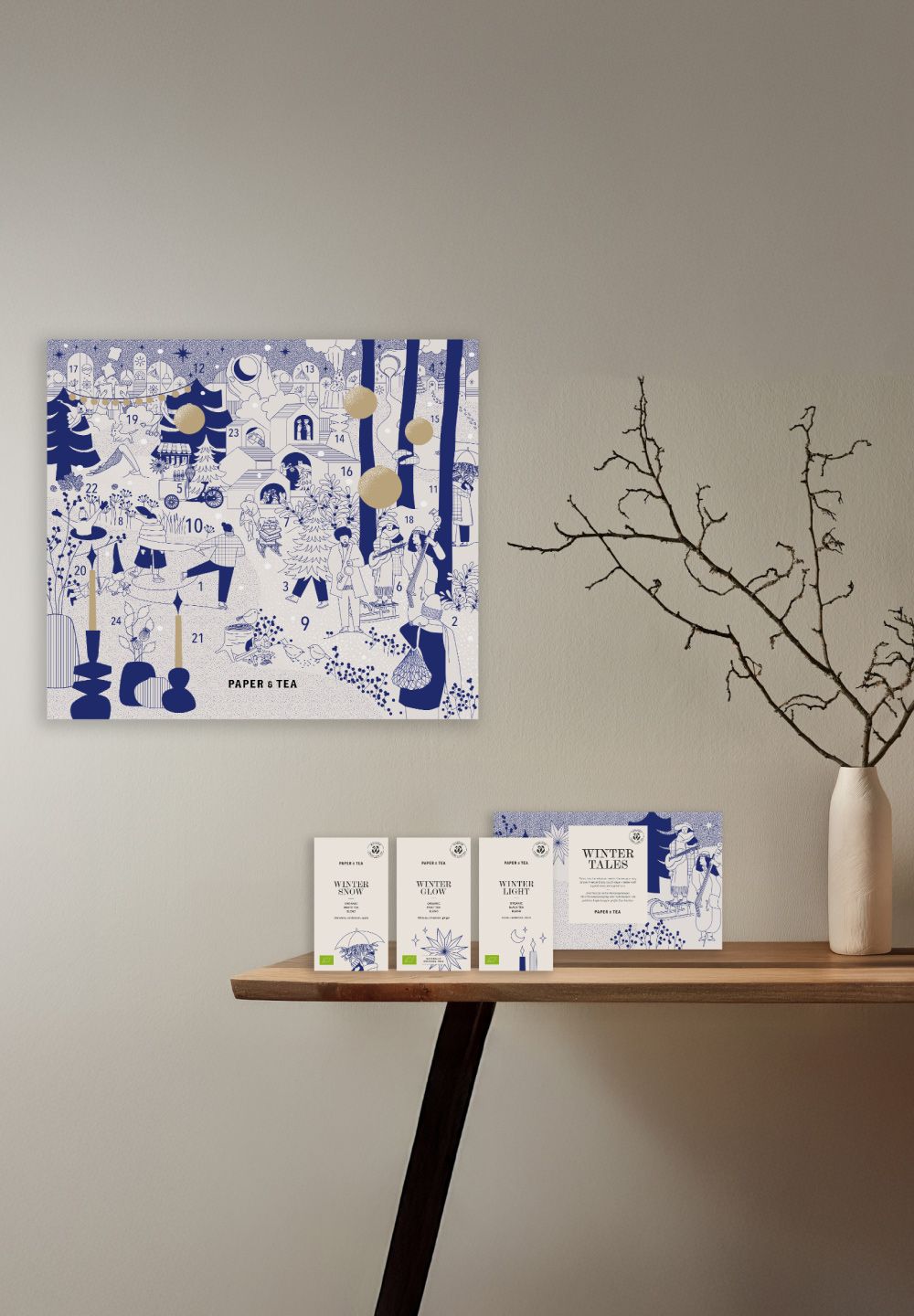 Blauer und weißer Tee-Adventskalender mit goldenen Details, vier Teeboxen auf Holztisch, weiße Vase.